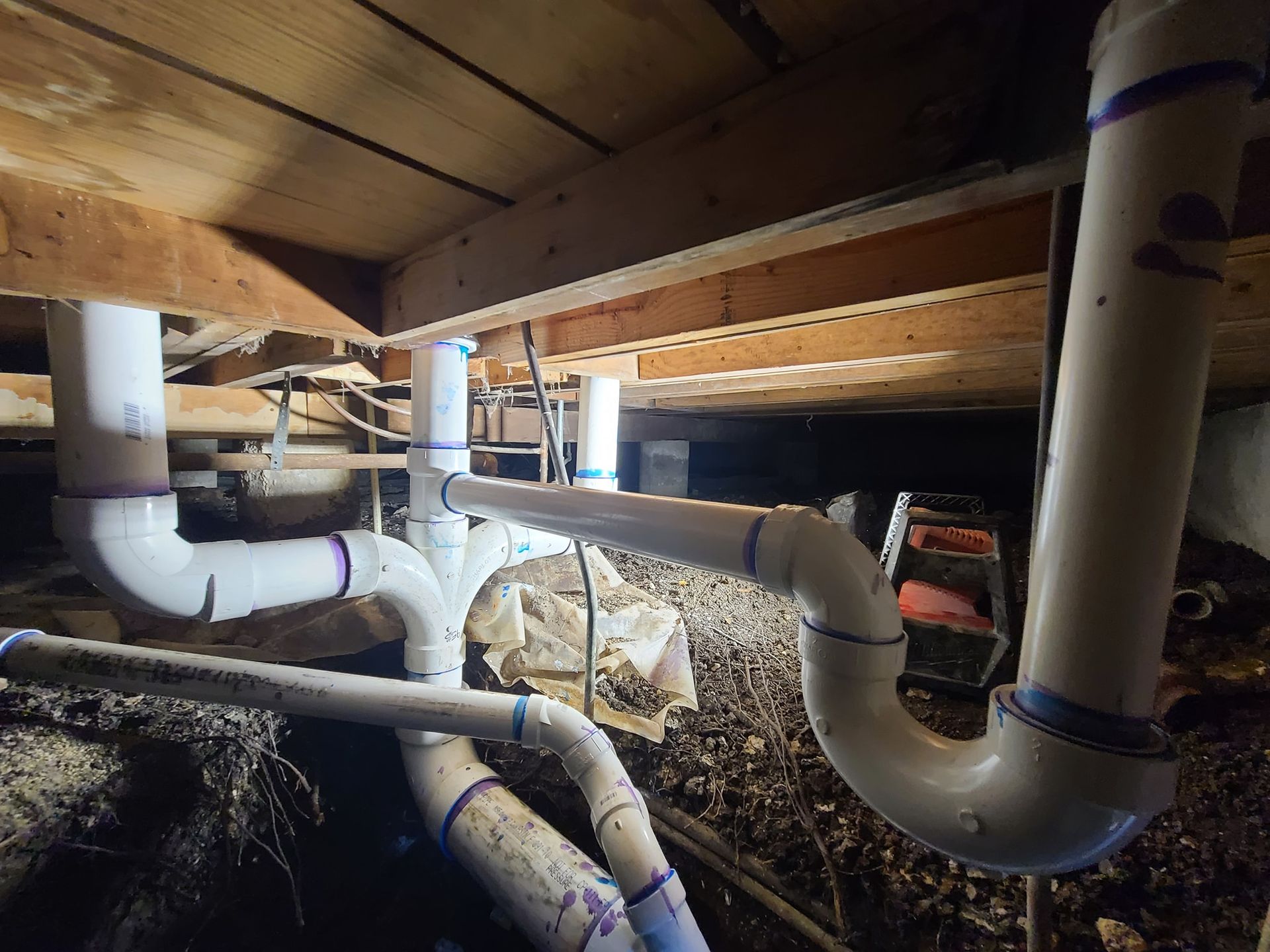 A bunch of pipes are under a wooden floor in a basement.