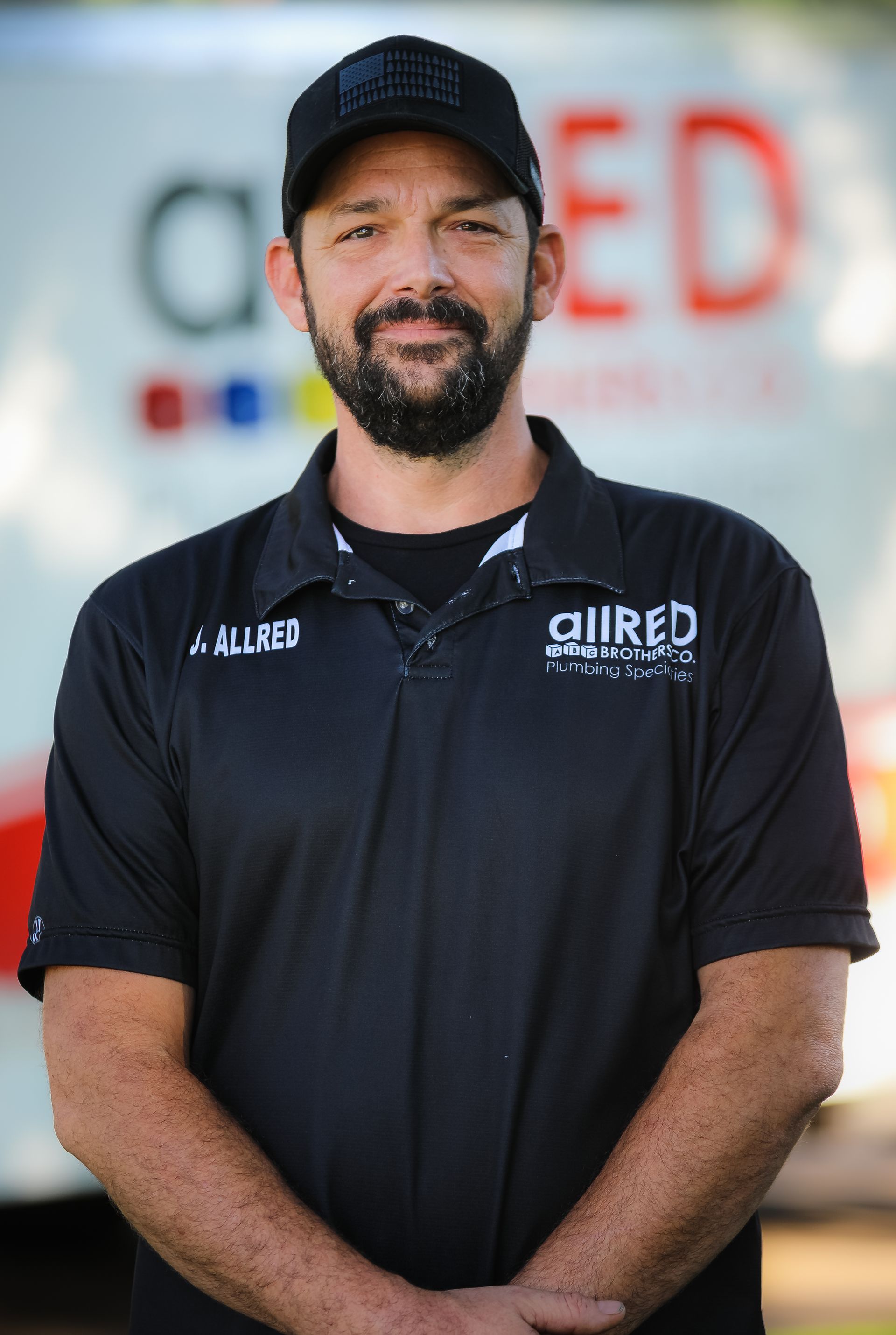 A man with a beard is wearing a black shirt and a hat.