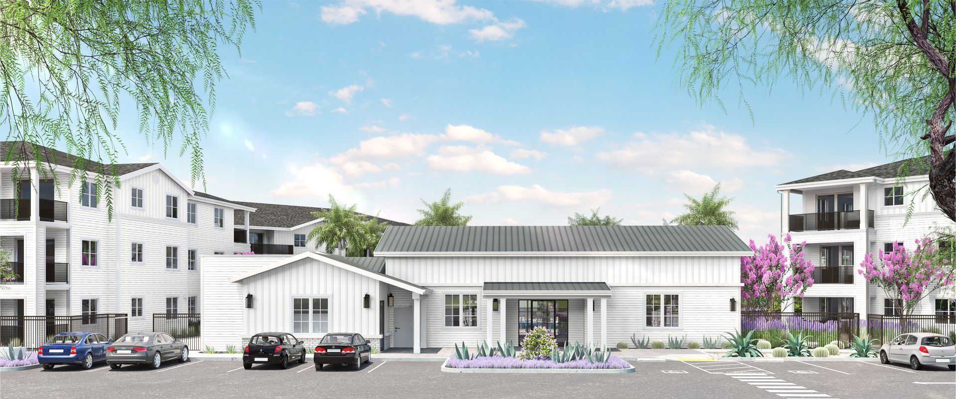 White buildings with dark roofs, cars parked in front, trees framing the sky.