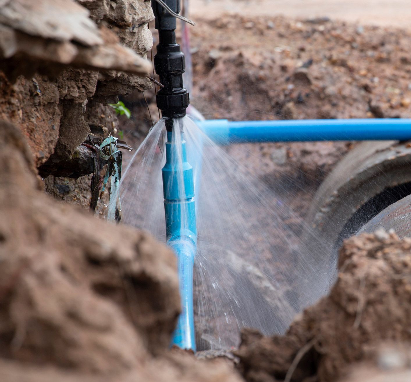 Leaking blue water pipe in a trench, water spraying out.