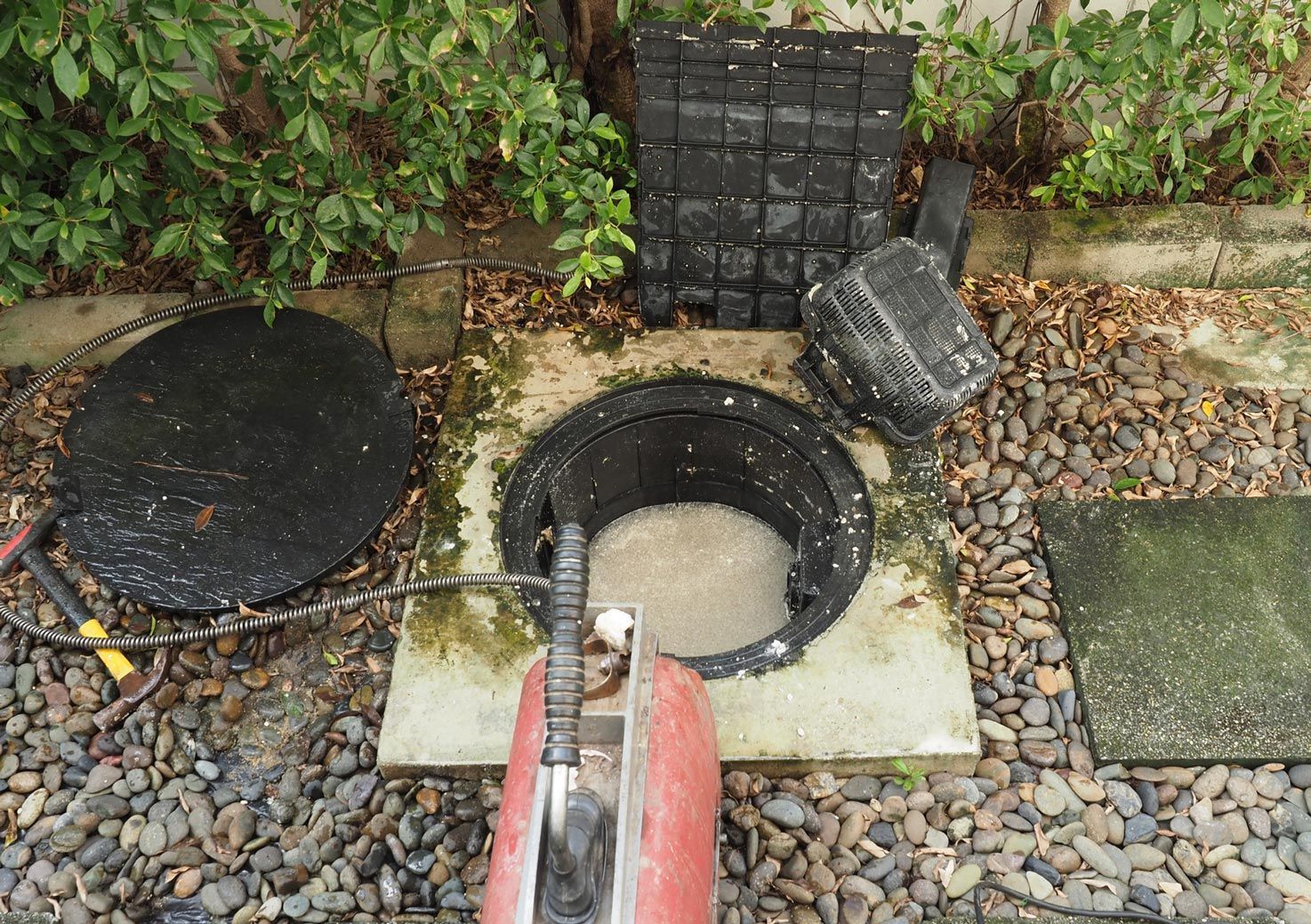 Open manhole surrounded by gravel and debris; maintenance in progress.