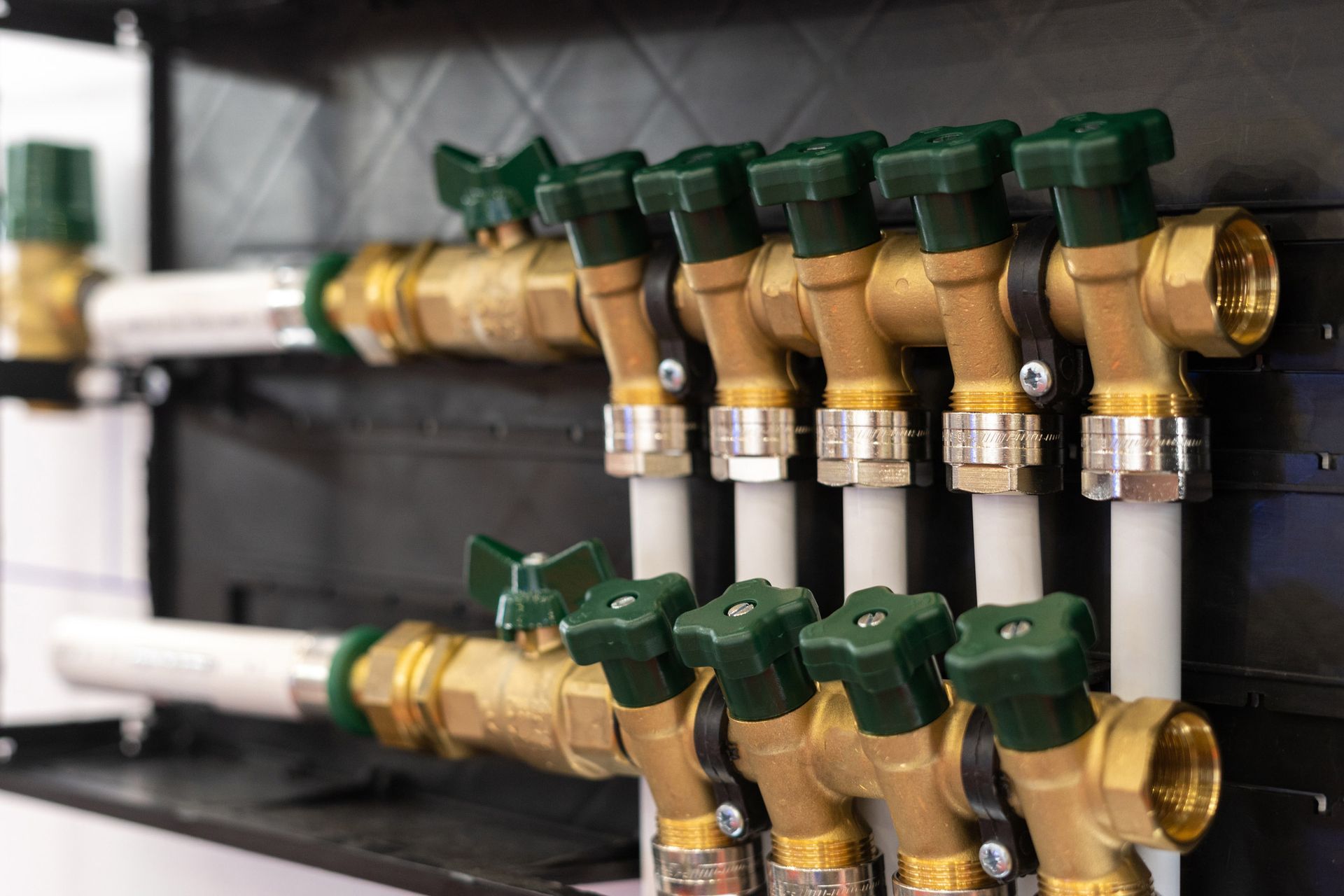 Brass manifold with green-handled valves and white pipes, mounted on a black panel.