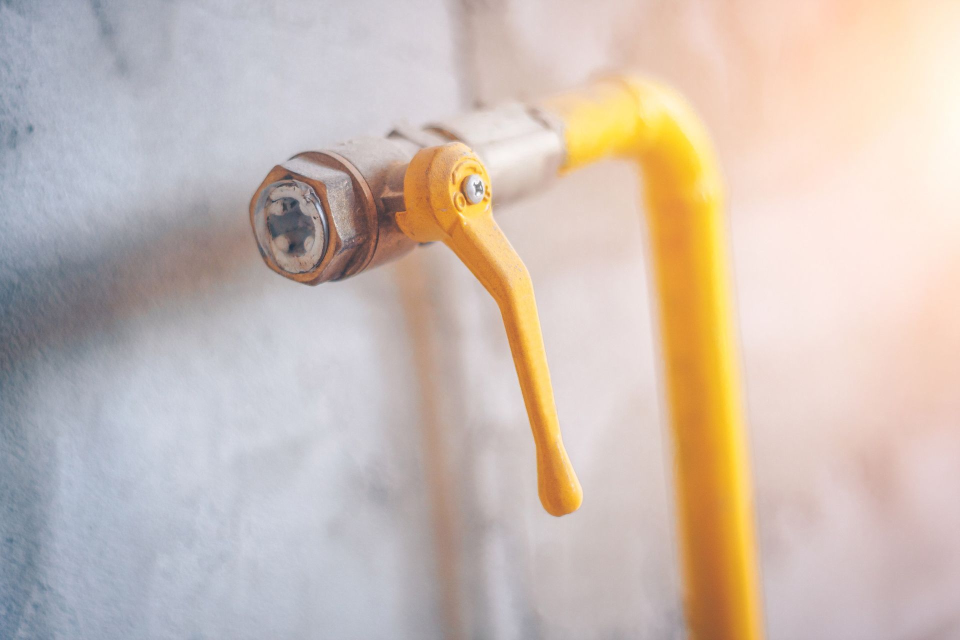 Yellow gas shut-off valve on a white wall, lever in the open position.