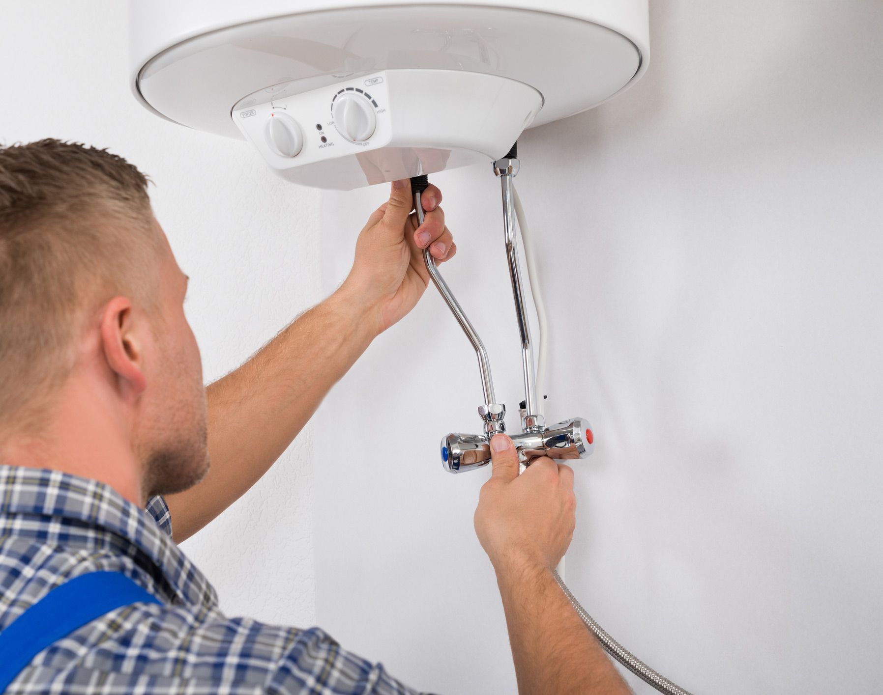 Plumber connecting water lines to a white tank-style water heater on a wall.