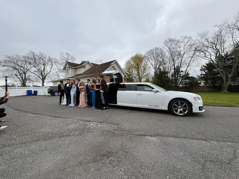 A group of people are standing in front of a white limousine.