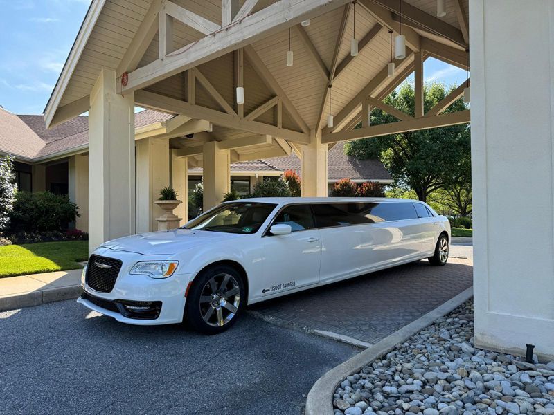 A white limousine is parked under a canopy in front of a building.
