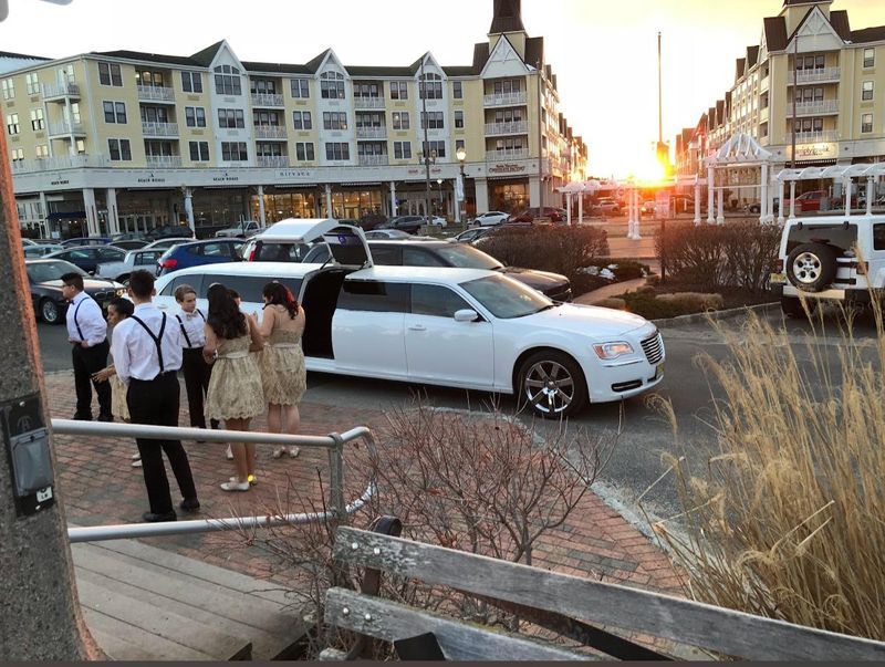 A group of people are standing in front of a white limousine.
