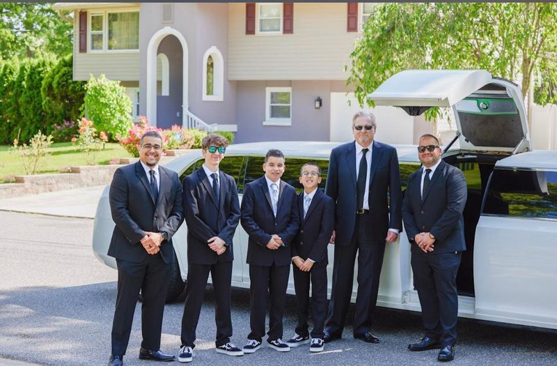 A group of men in suits and ties are standing in front of a white limousine.