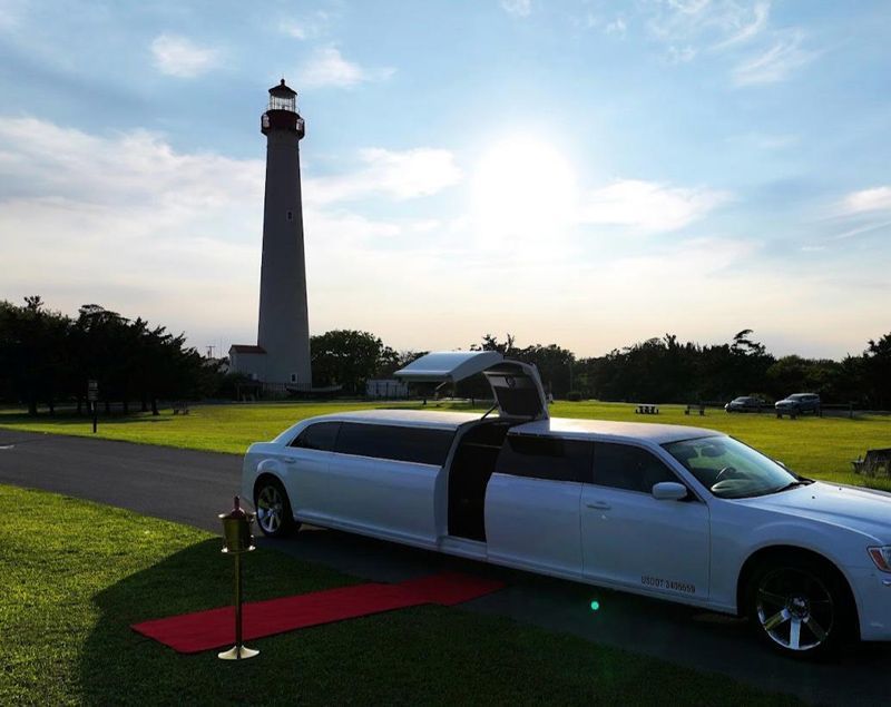 A white limousine is parked in front of a lighthouse