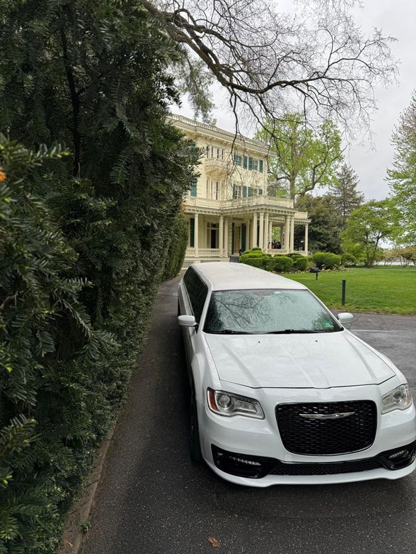 A white limousine is parked in front of a large house.
