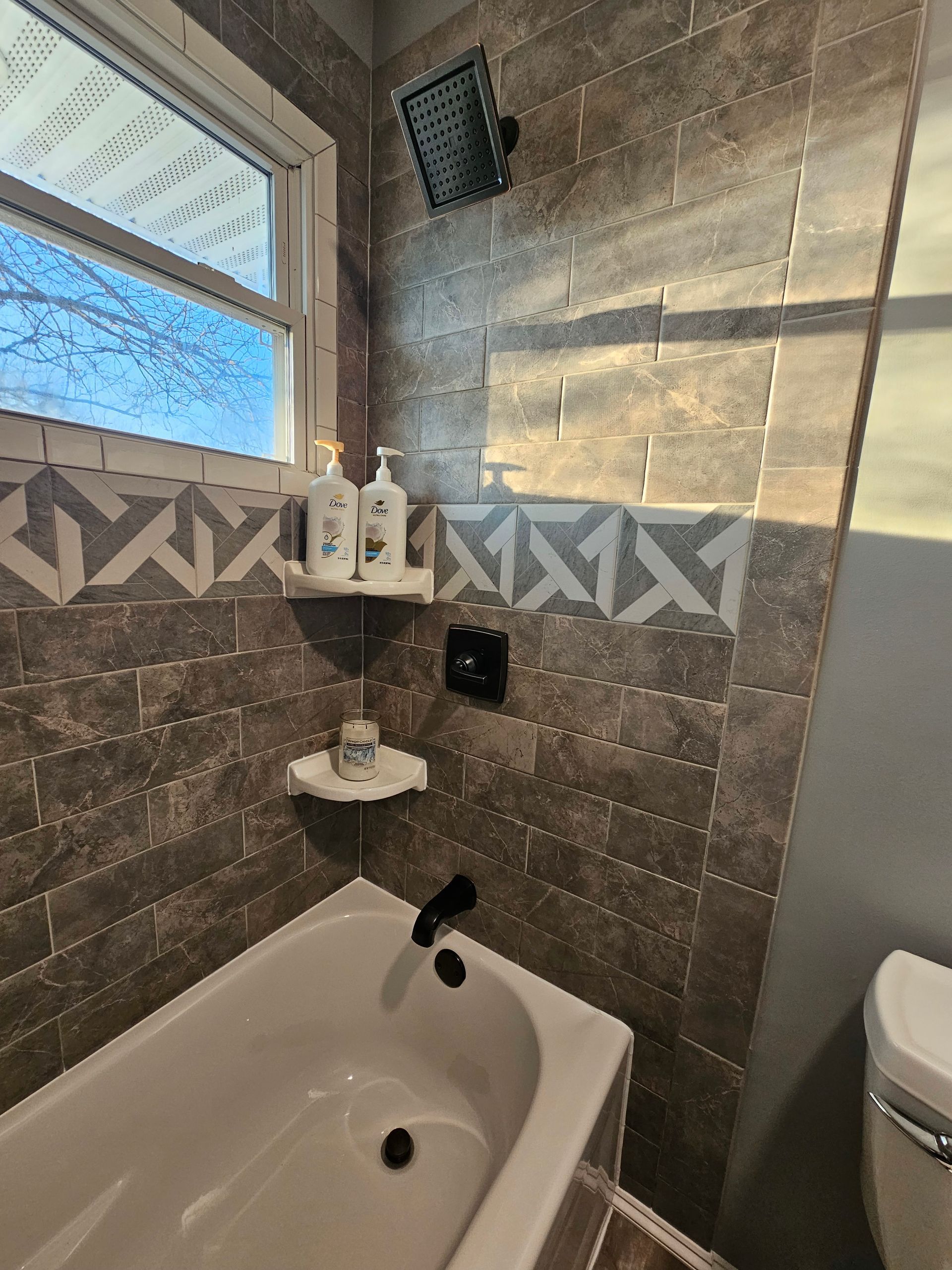 A bathroom with a tub , toilet , shower and window.