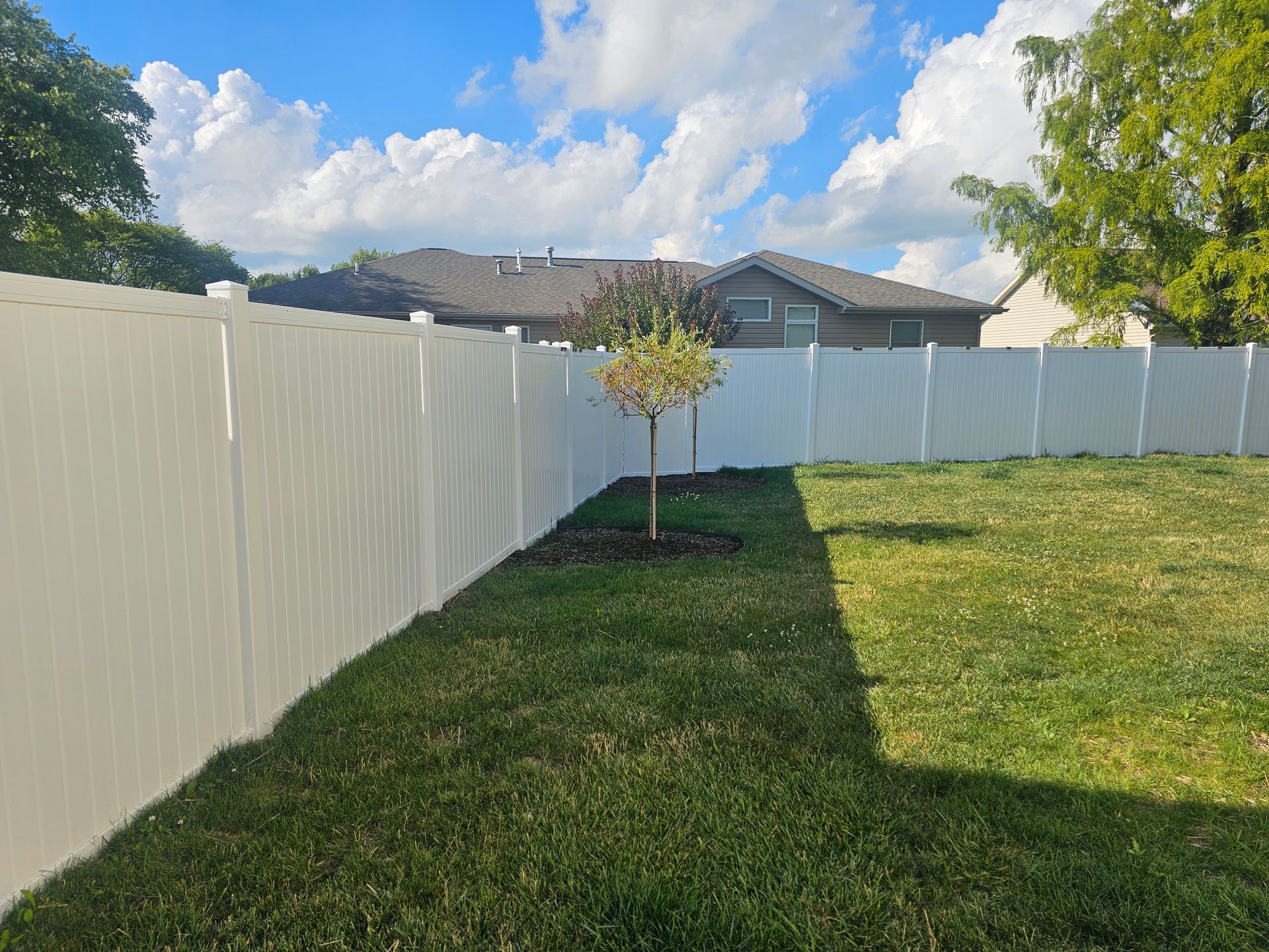 A white fence surrounds a lush green yard with a tree in the middle.