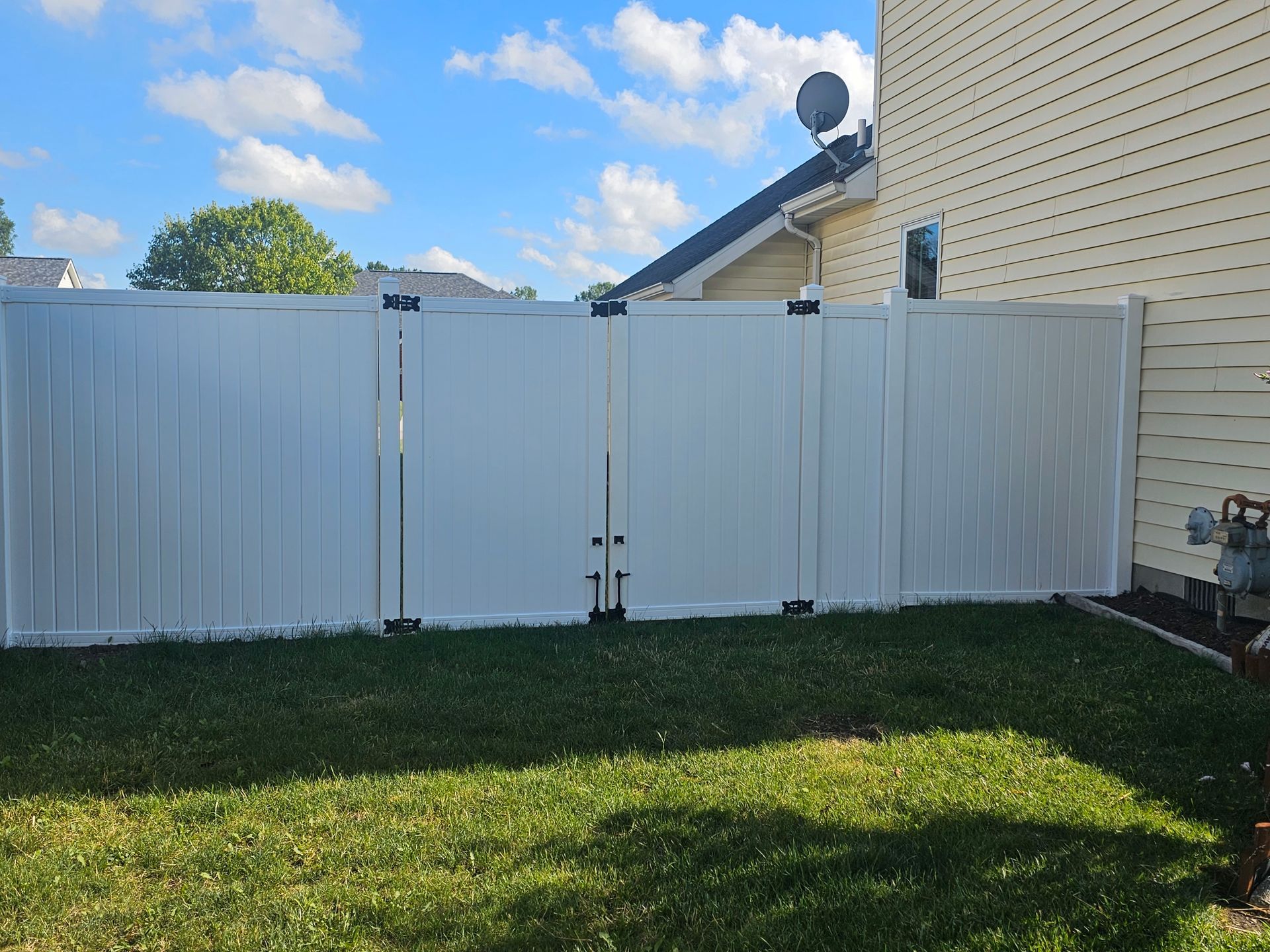 A white fence is in the backyard of a house.