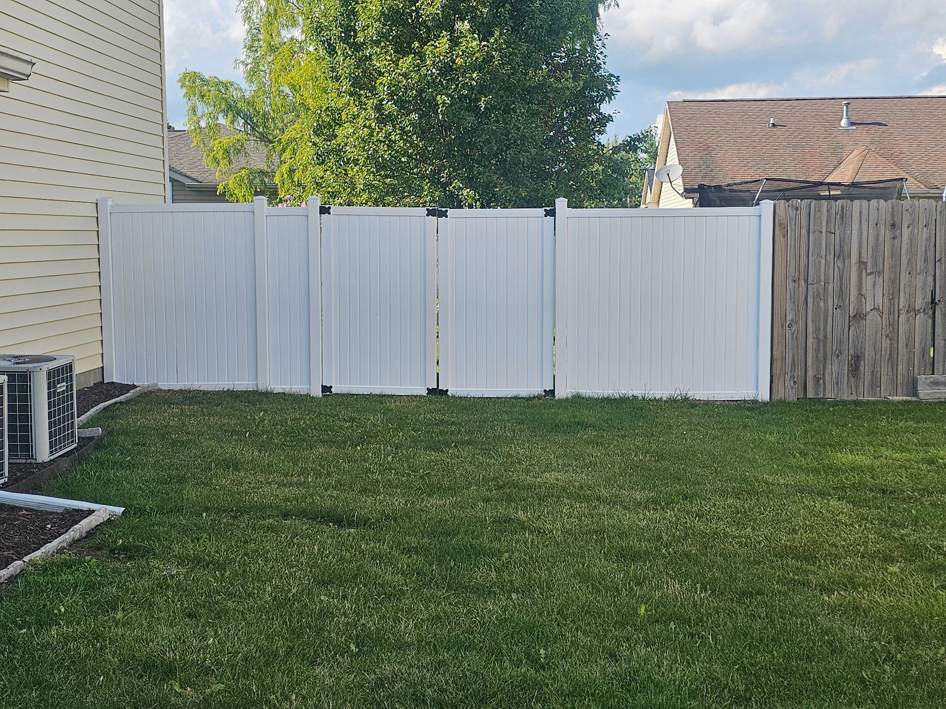 A backyard with a white fence and a wooden fence.