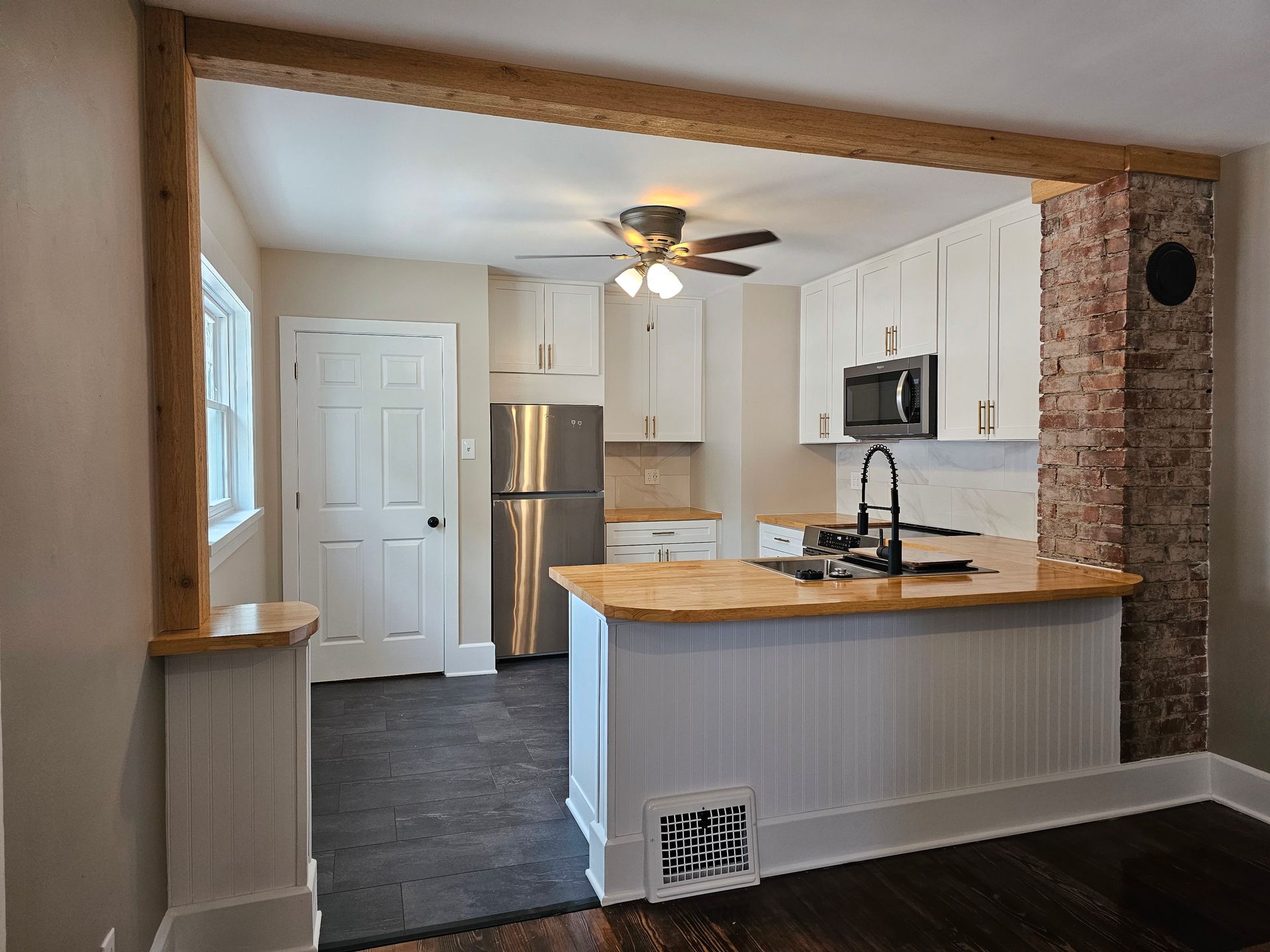 A kitchen with white cabinets , a stainless steel refrigerator , a microwave , and a ceiling fan.