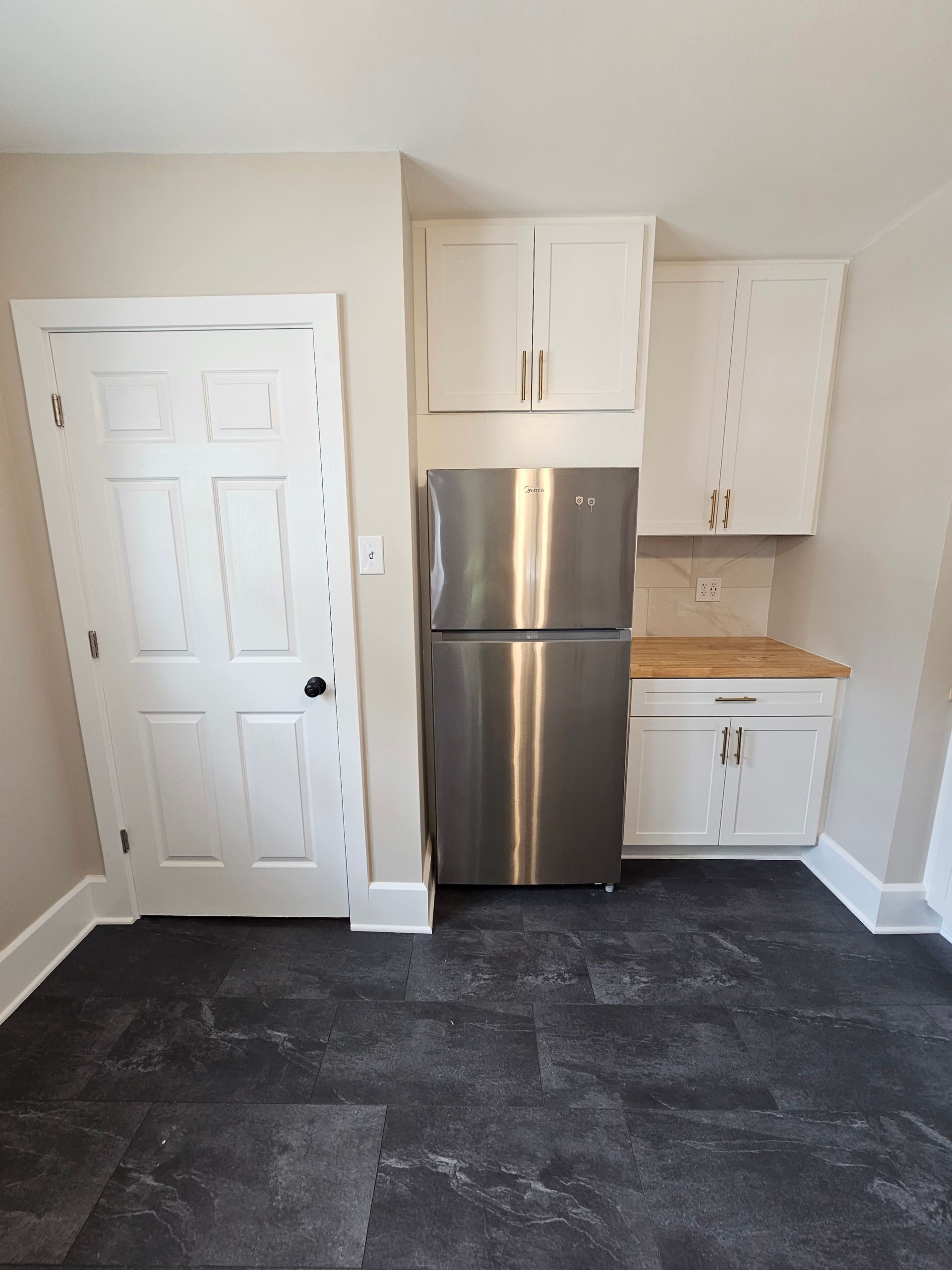 An empty kitchen with a stainless steel refrigerator and white cabinets.