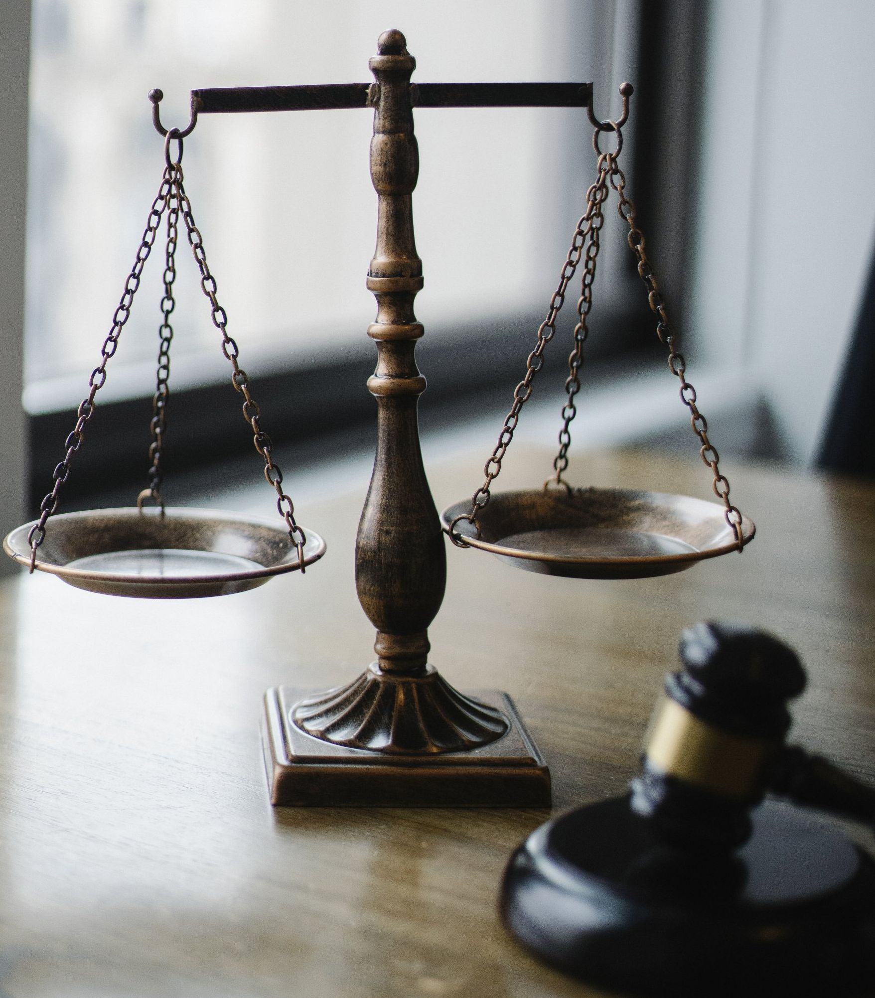 a scale of justice sits on a wooden table next to a gavel