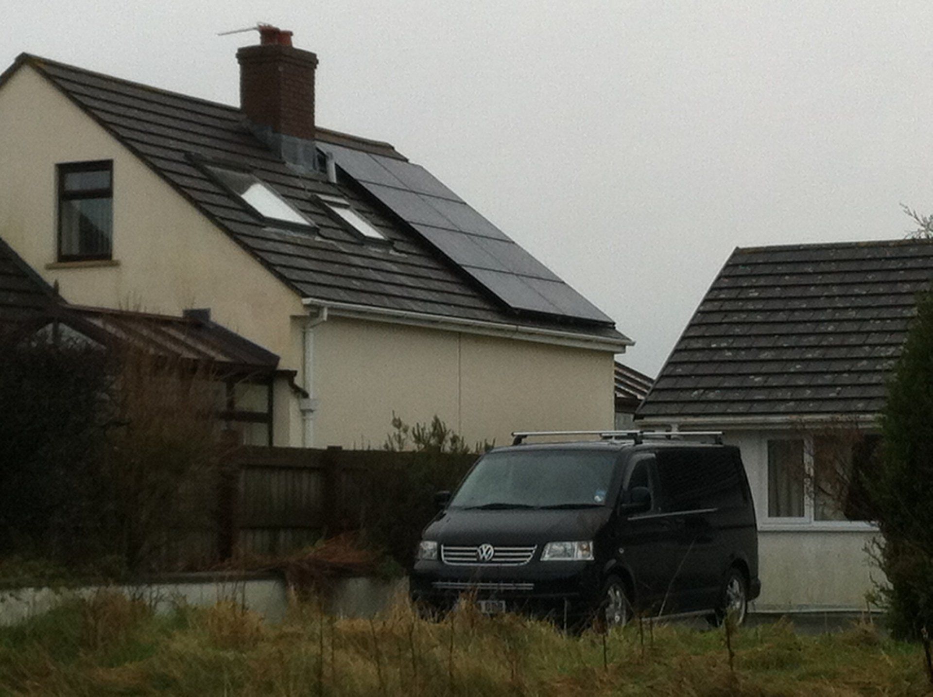 van in foreground with solar panels on roof of house
