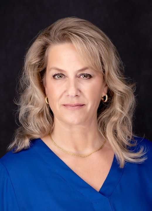 A woman wearing a blue shirt and earrings is standing in front of a black background.