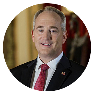 Man in a suit smiles at the camera, red tie, oval frame.