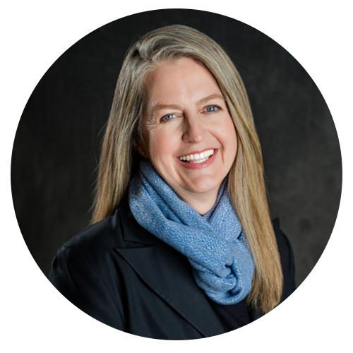 Woman with long blonde hair, smiling, wearing a blue scarf and black blazer.