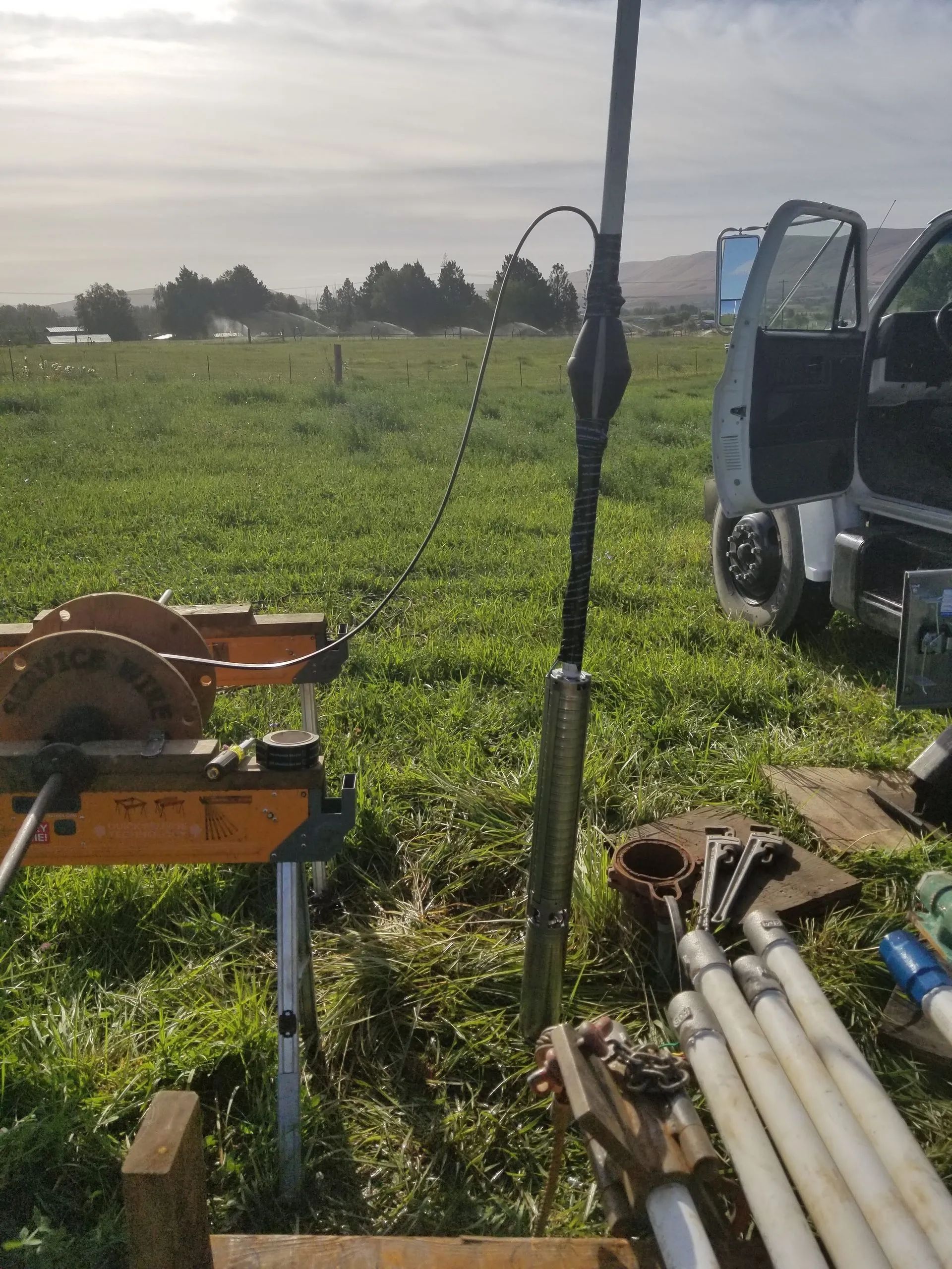 Well drilling equipment set up in a grassy field; includes pipes, truck, and drill.