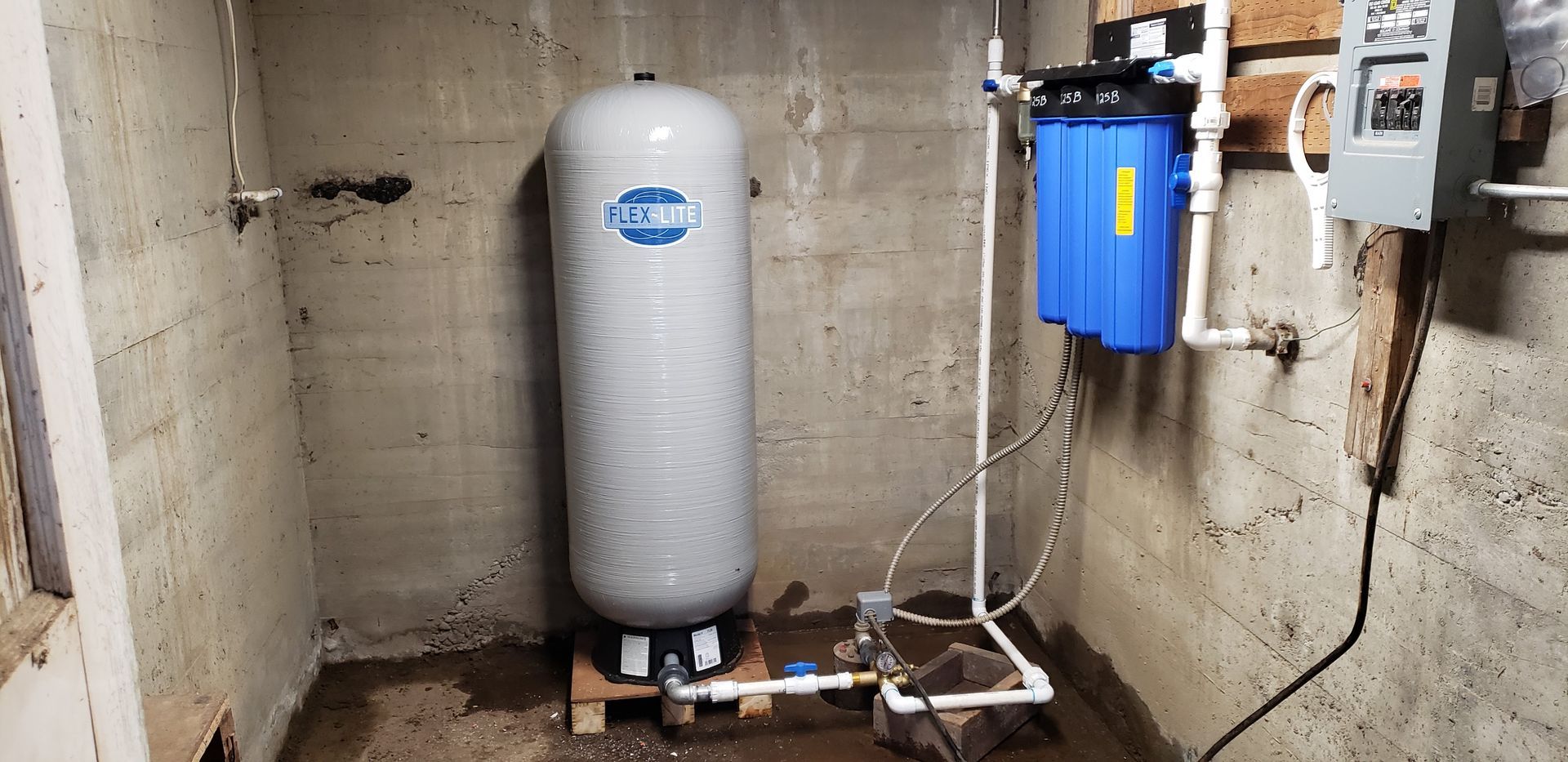 A water tank is sitting in a basement next to a water filter.