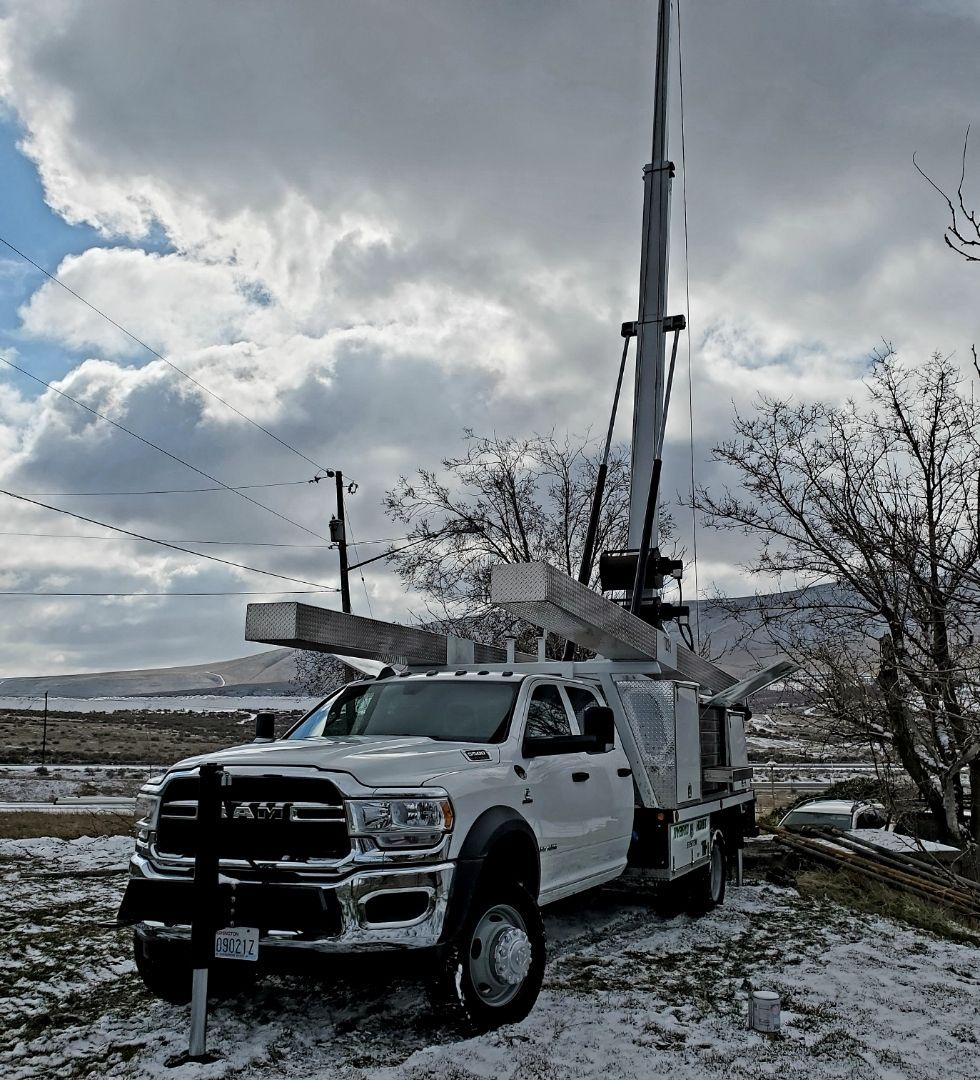 A white truck with a crane on top of it is parked in the snow.