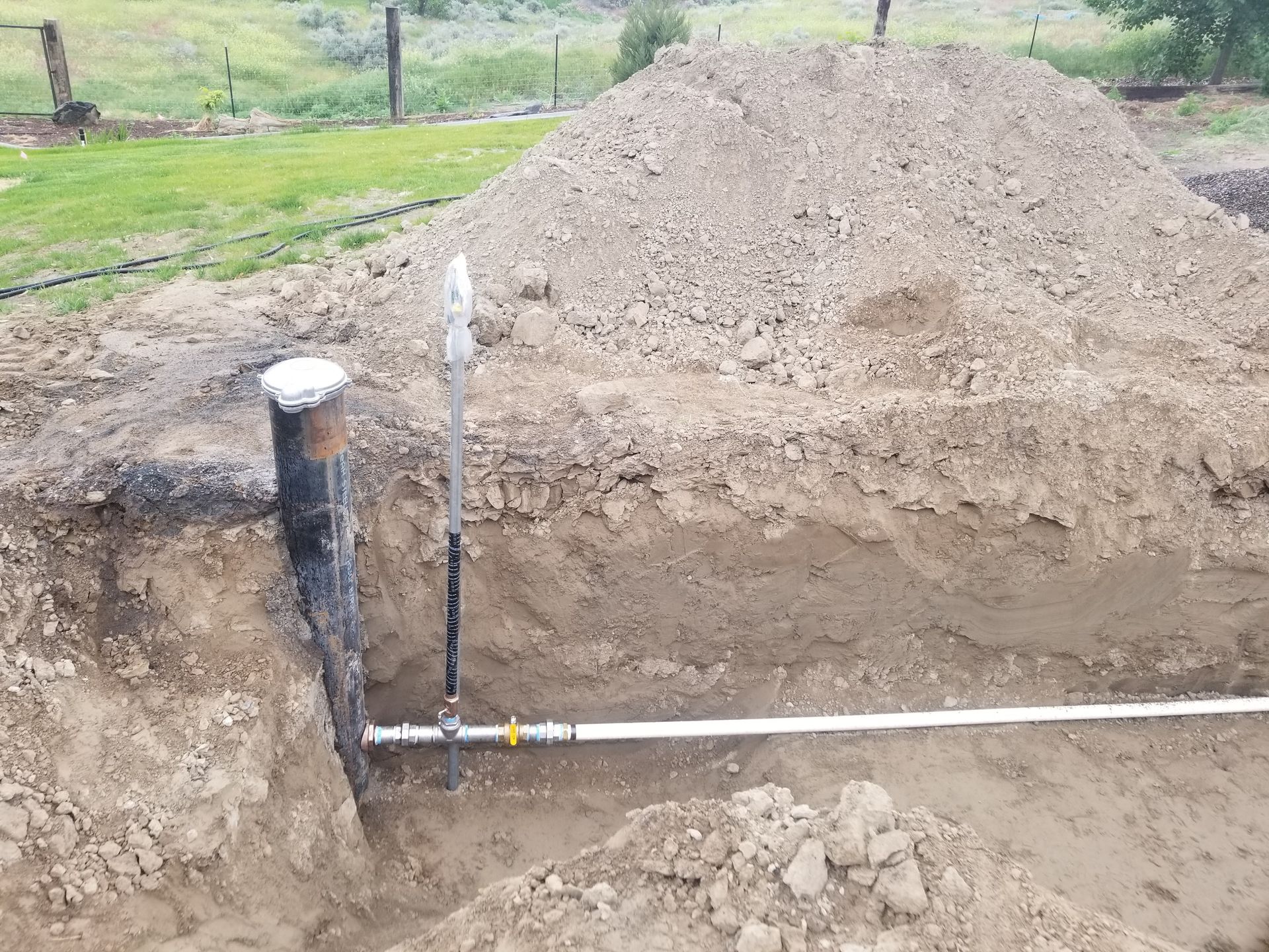A pipe is being installed in the dirt next to a pile of dirt.