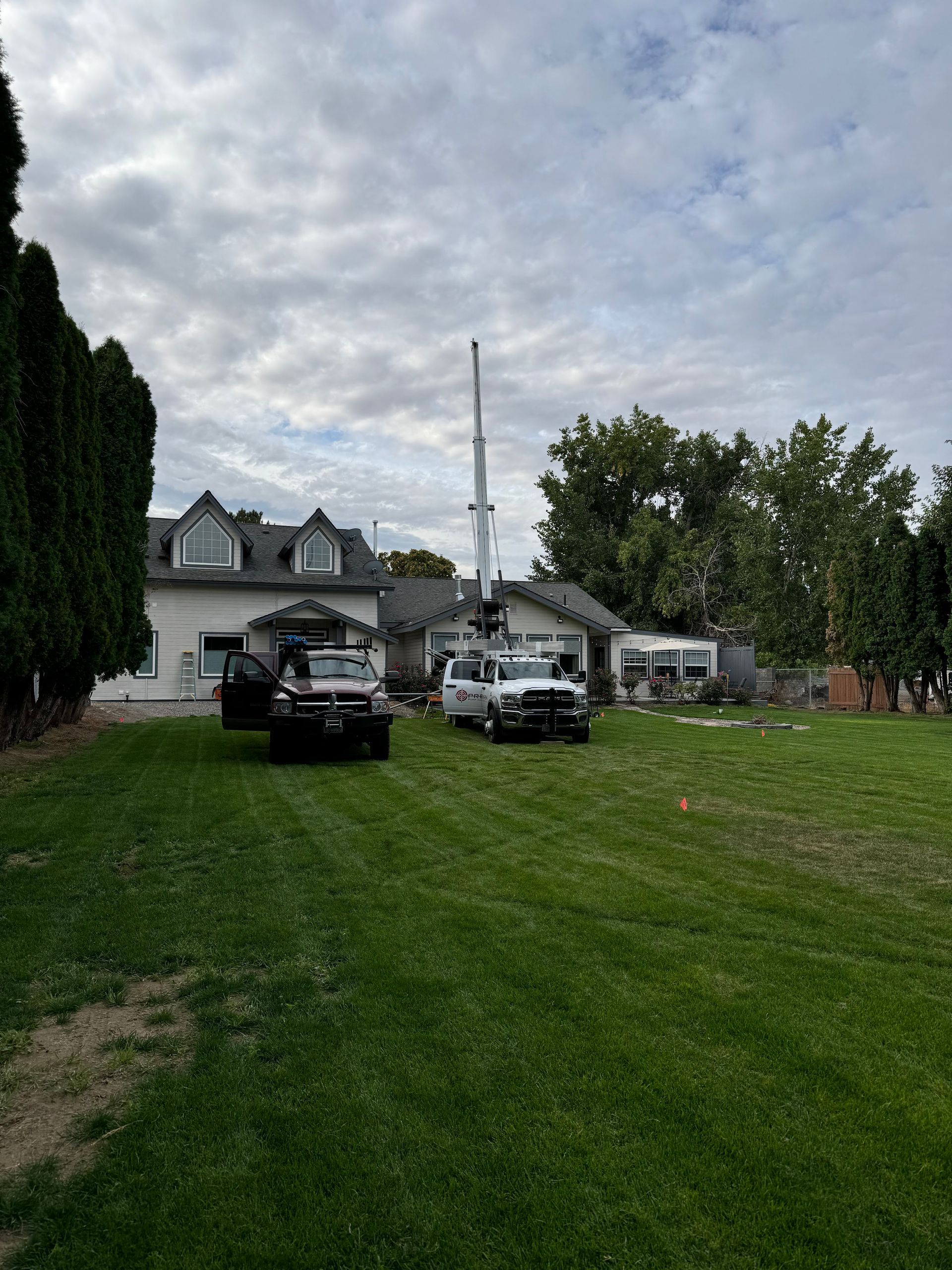 Two trucks are parked in a grassy field in front of a house.