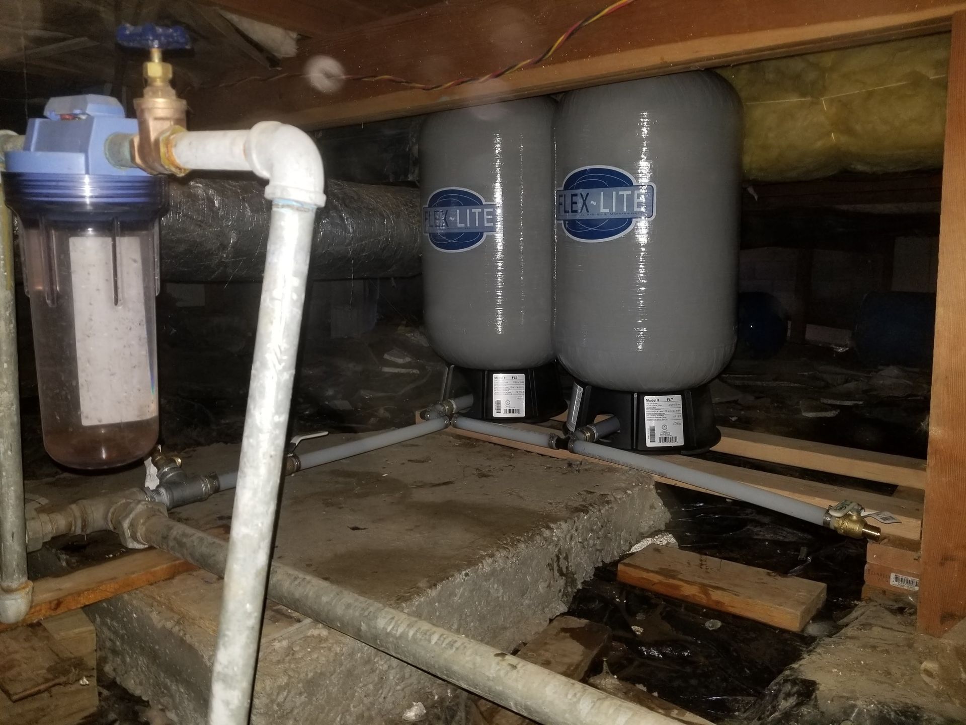 Two water tanks are sitting under a wooden ceiling in a basement.