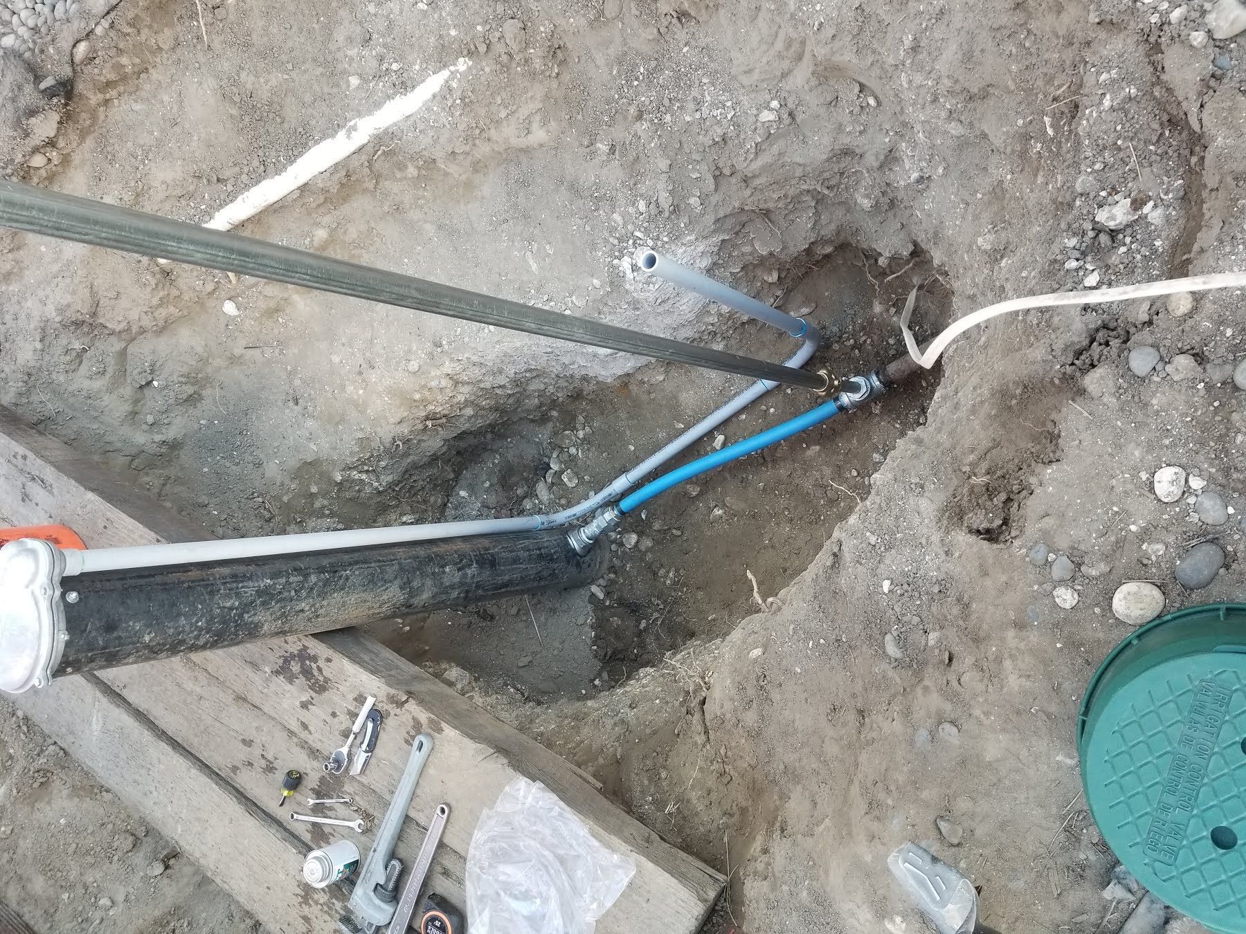 A person is cutting a pipe with a hacksaw in the dirt.