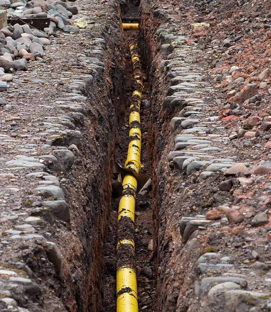 Yellow Pipe Laid in a Trench Dug in Brown Soil, Surrounded by Stones — Atherton Location Services In Atherton, QLD