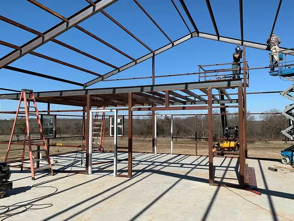 Workers build a metal-framed structure with an open second-story deck under a clear blue sky.