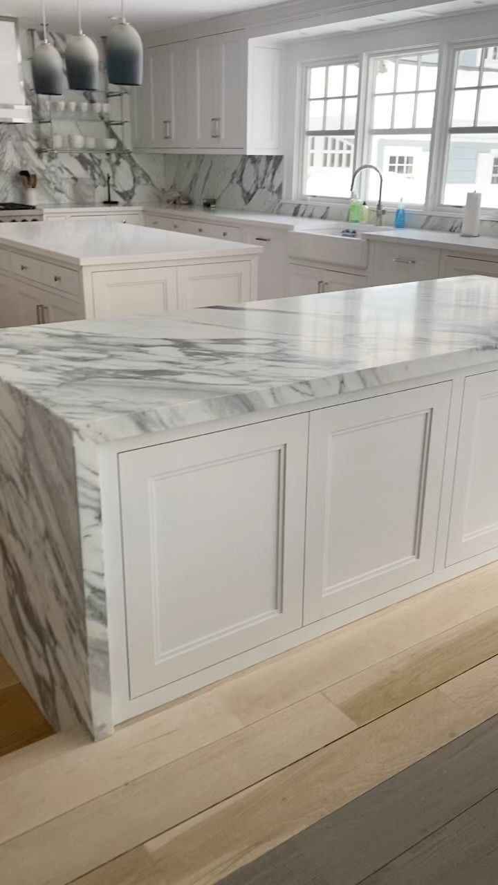 White kitchen with marble countertops, wood cabinets, and large island.