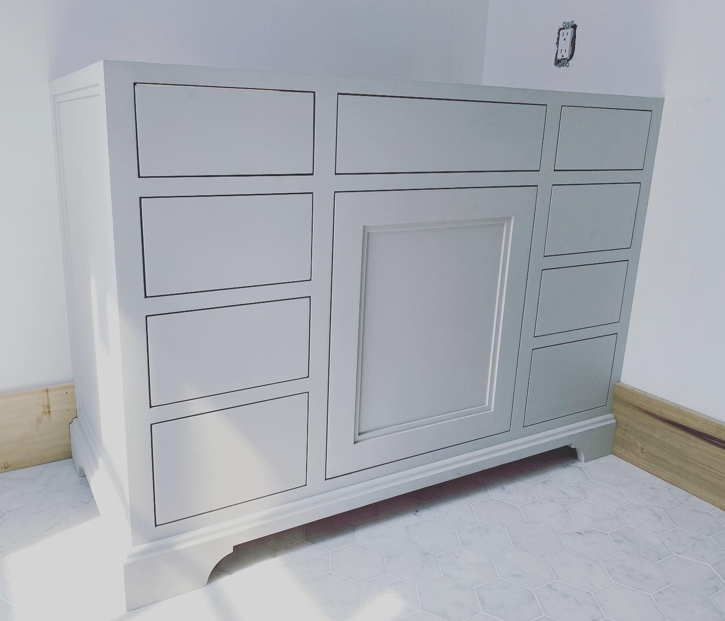 White bathroom vanity with drawers and a door, installed in a room with white walls and a light-colored floor.