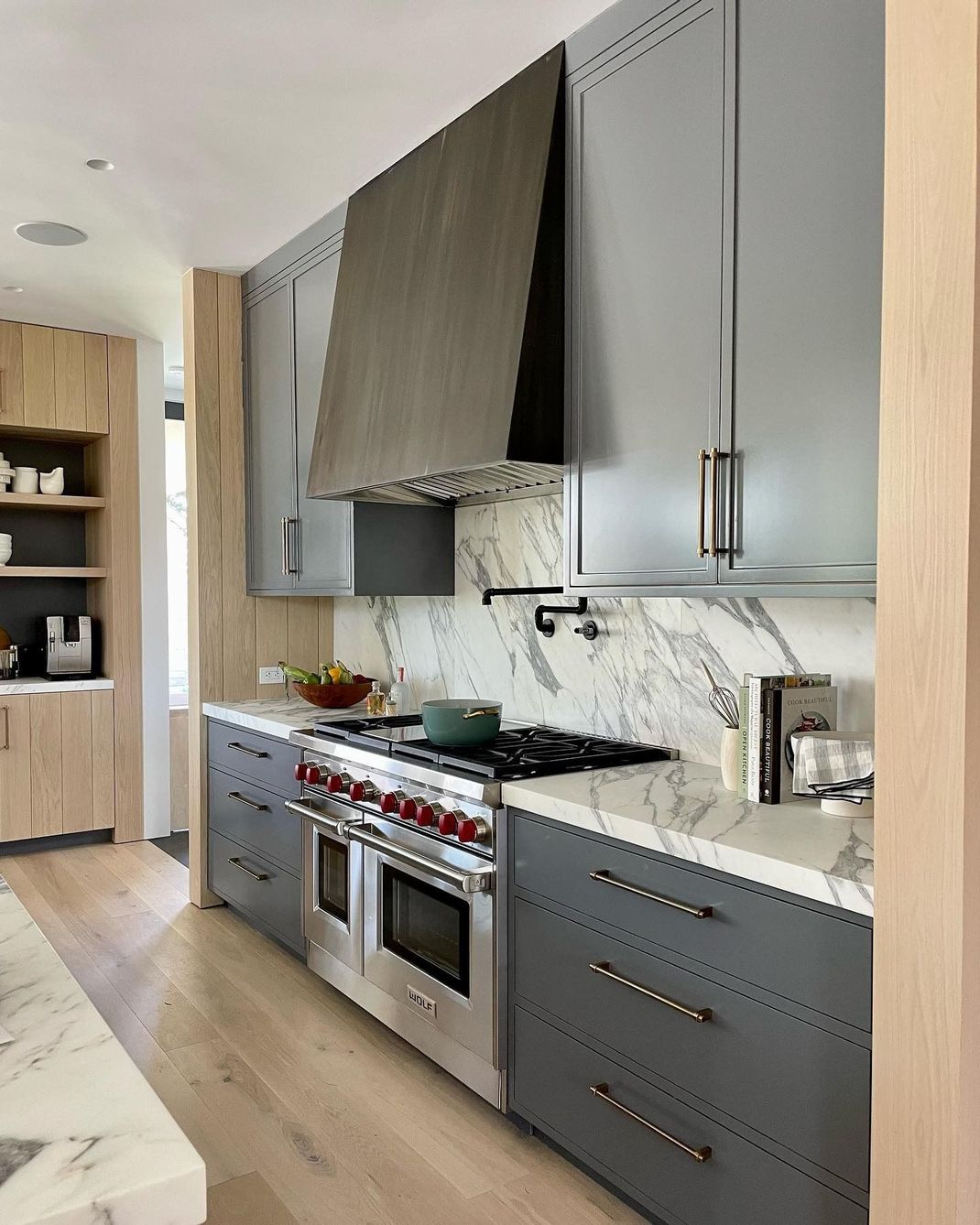 Modern kitchen with grey cabinets, marble backsplash, stainless steel oven/range, and wood accents.
