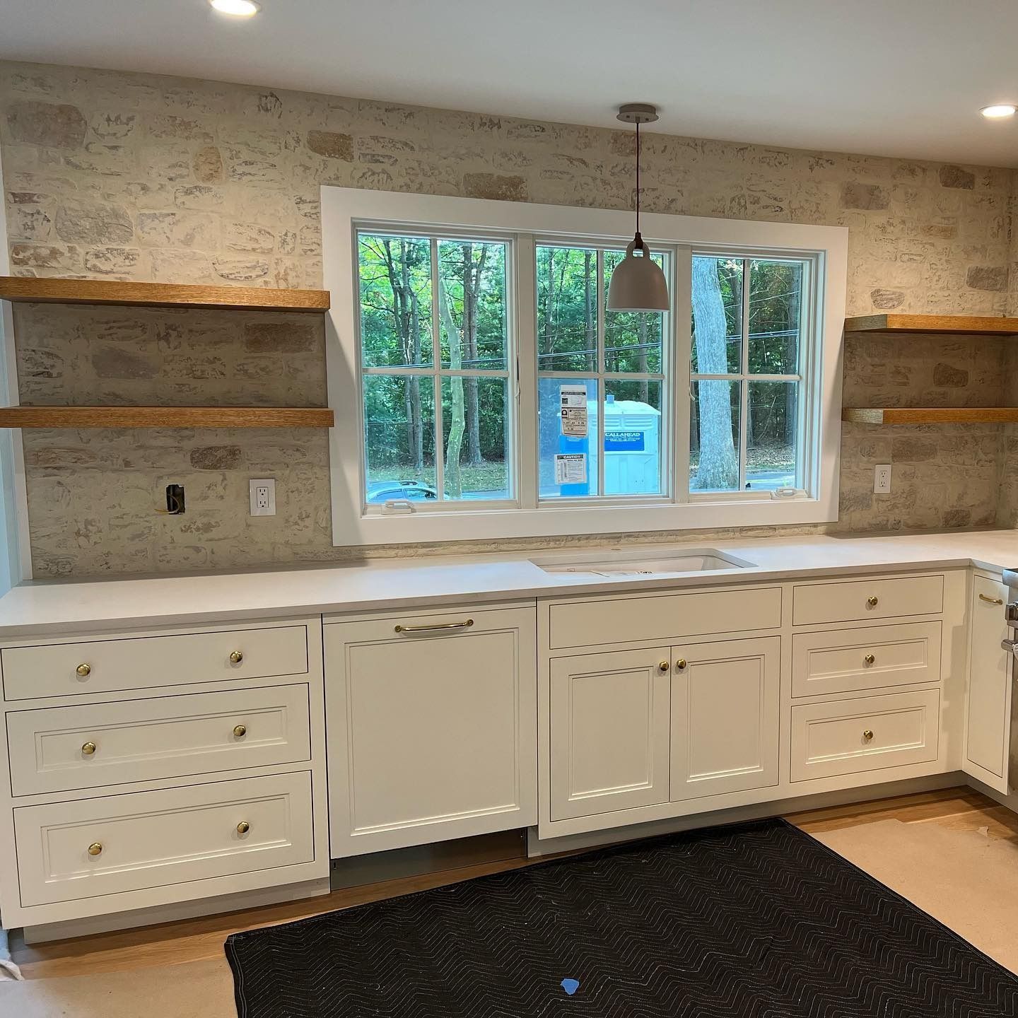 White kitchen with cabinets, open shelves, window, and textured wall.