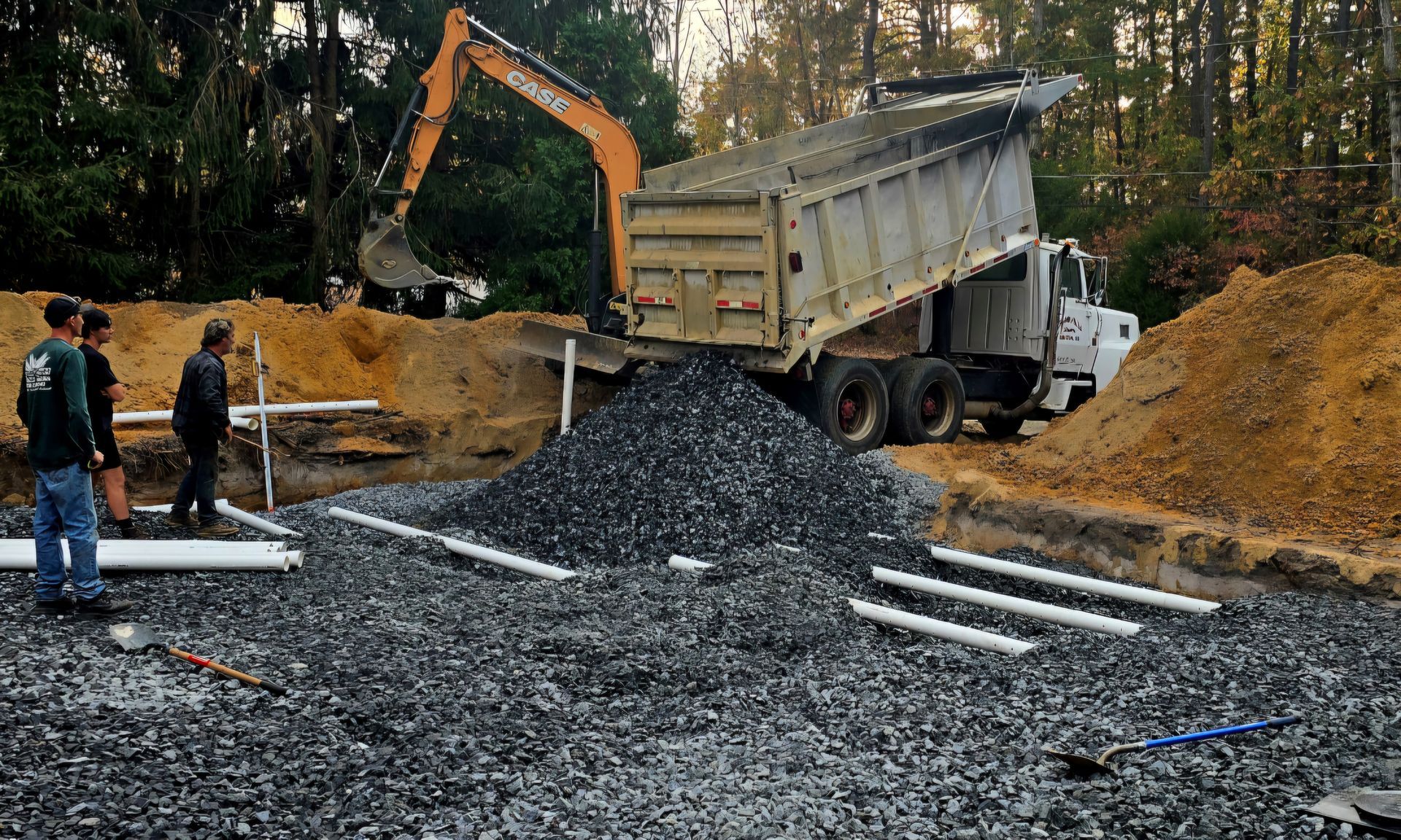 A large concrete cylinder is being lifted into a hole with a bulldozer in the background