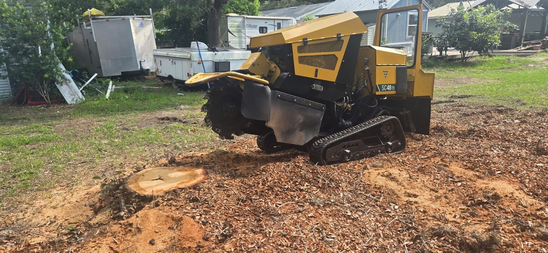 A yellow stump grinder on tracks grinding a tree stump in a yard.