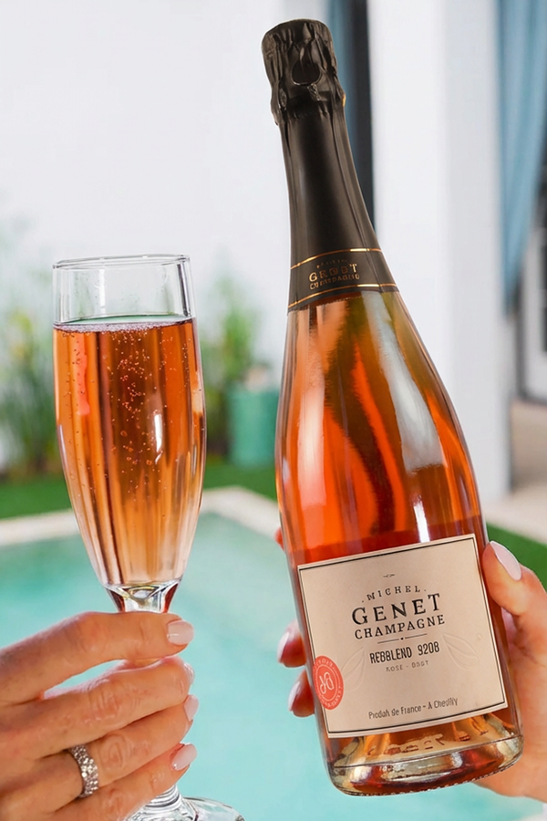 Champagne bottle and glass, both filled with pink liquid, held by two hands near a pool.