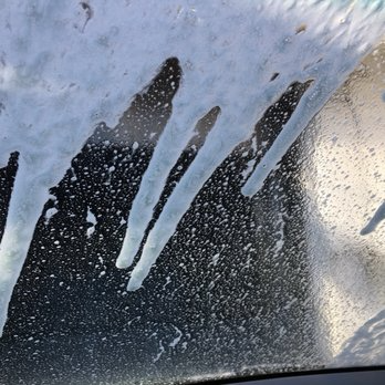 Windshield covered in soap streaks and suds at a car wash.