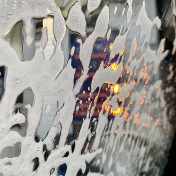 Car wash window covered in soapy foam, obscuring view of blurred lights.