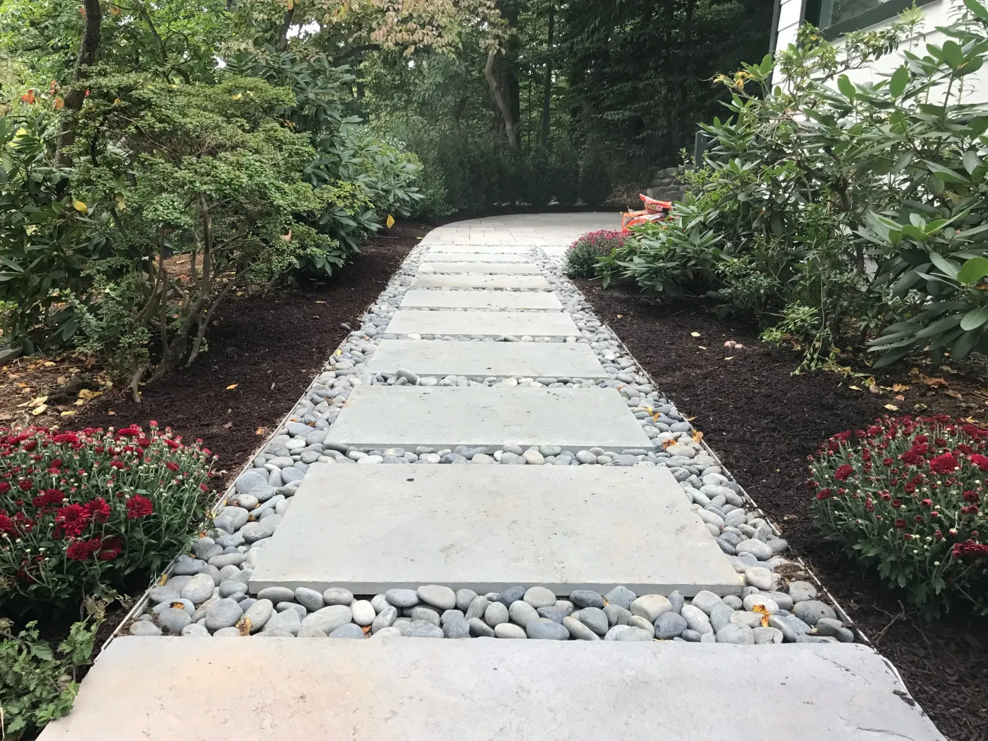 Concrete pavers pathway lined with gravel and blooming bushes in a garden.
