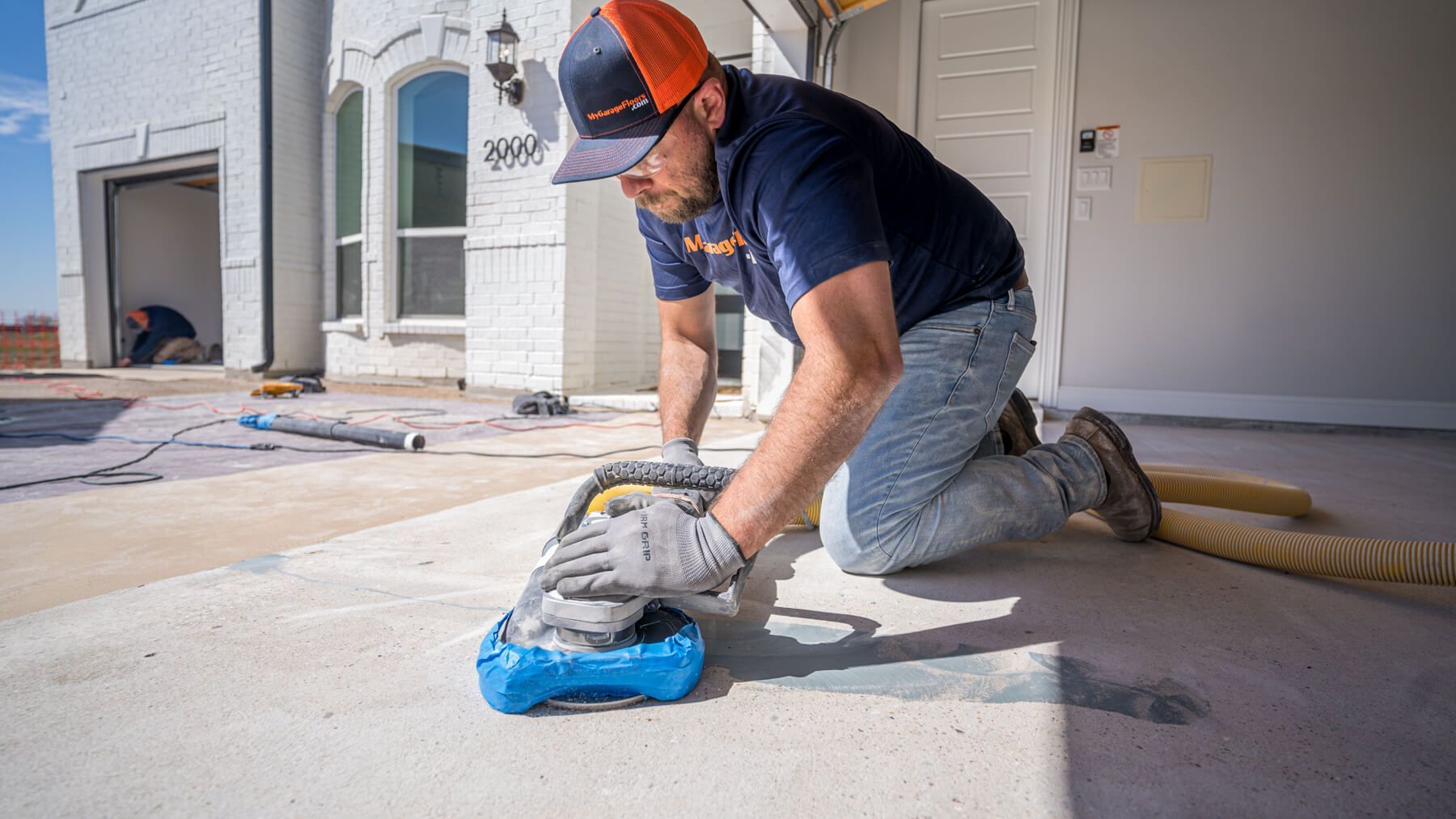 Person kneeling, sanding concrete outside a house; blue and orange colors.