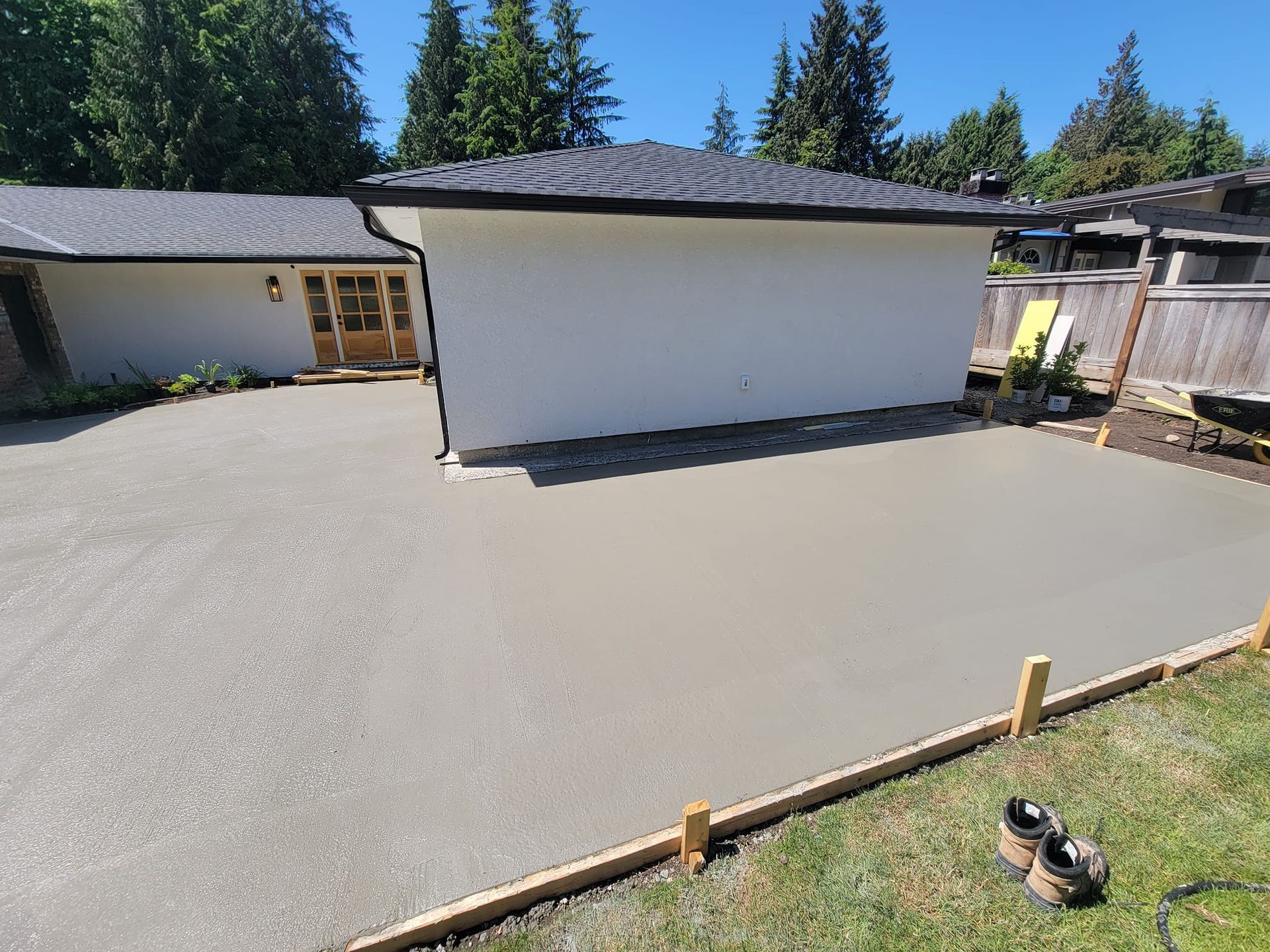 Newly poured concrete patio next to a white building with a black roof and a wooden frame.