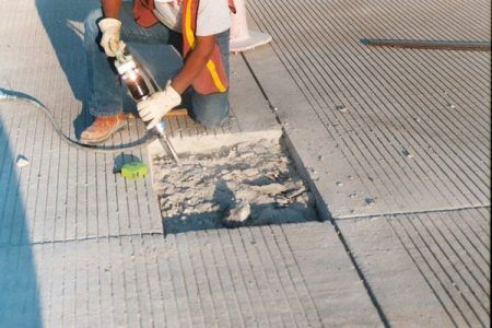 Person filling a square cut in concrete road with sealant, wearing gloves and safety vest.