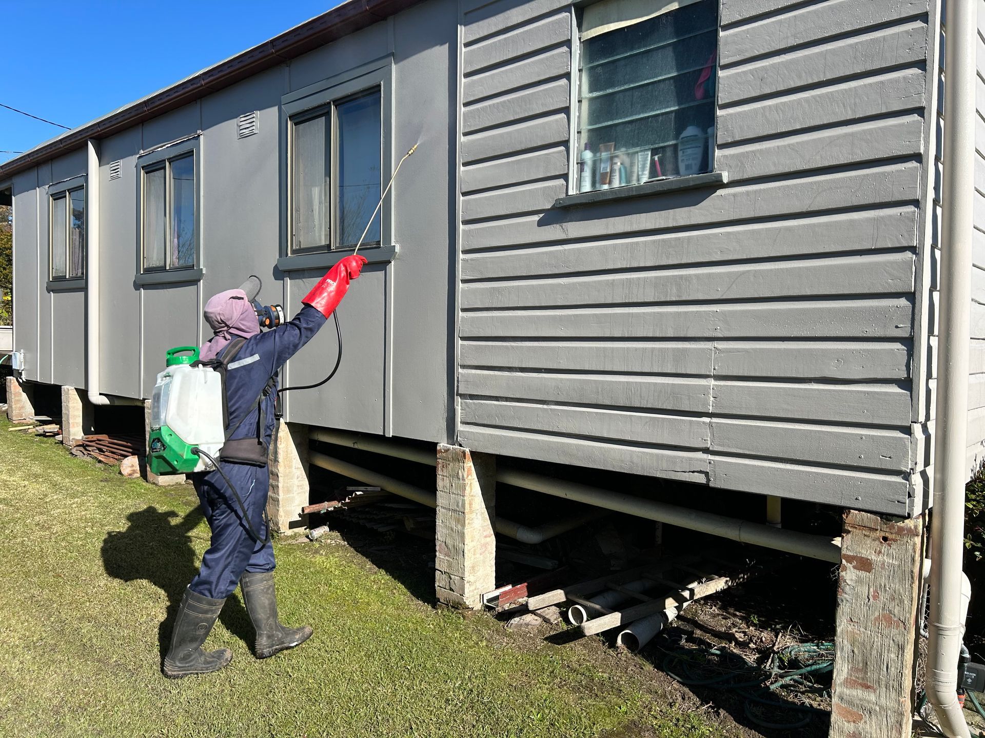 A Man is Spraying a Wooden Floor With a Sprayer — Precision Pest Services in Wherrol Flat, NSW