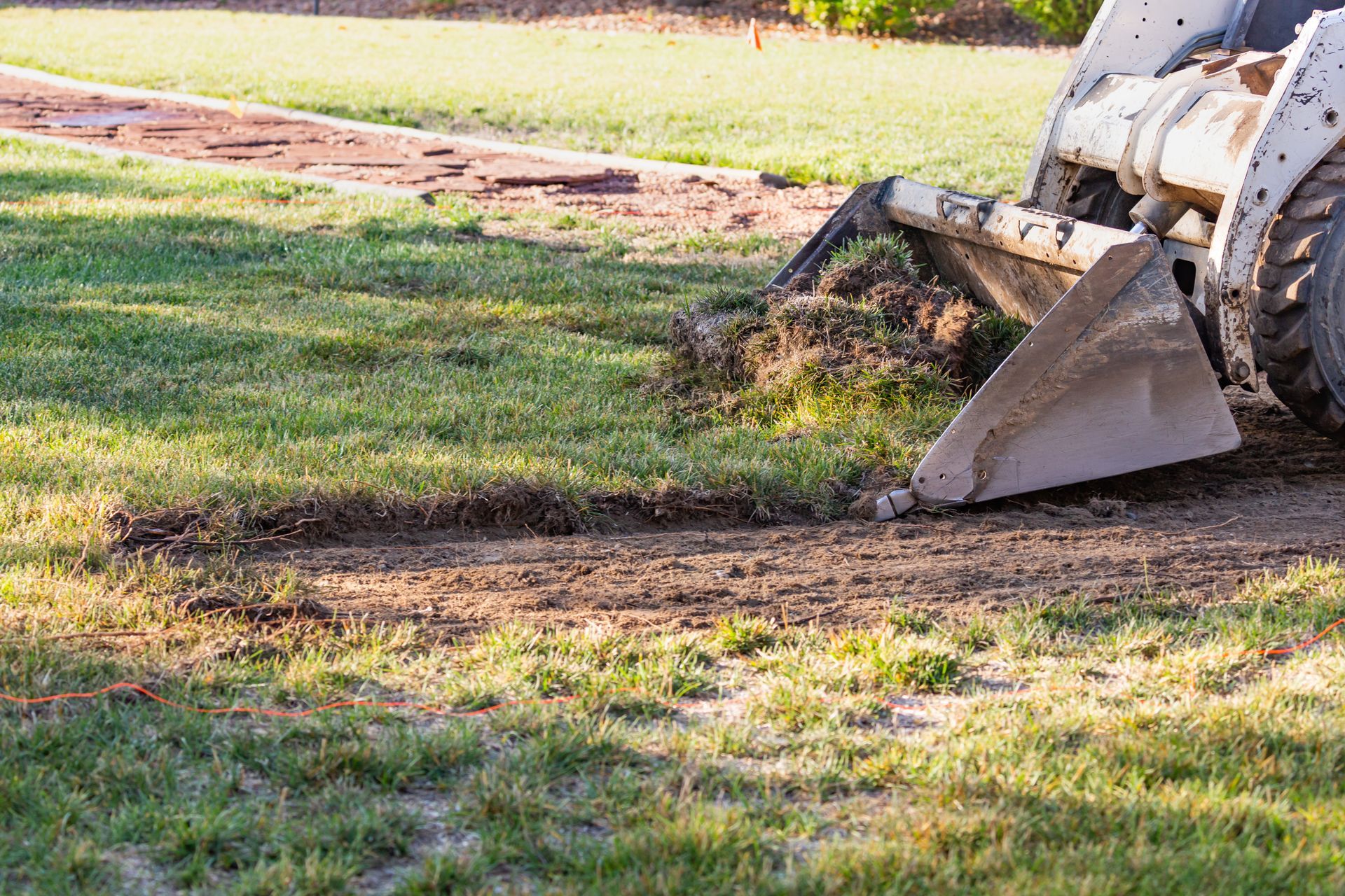 A small bulldozer in a yard, removing grass to prepare for a pool installation.