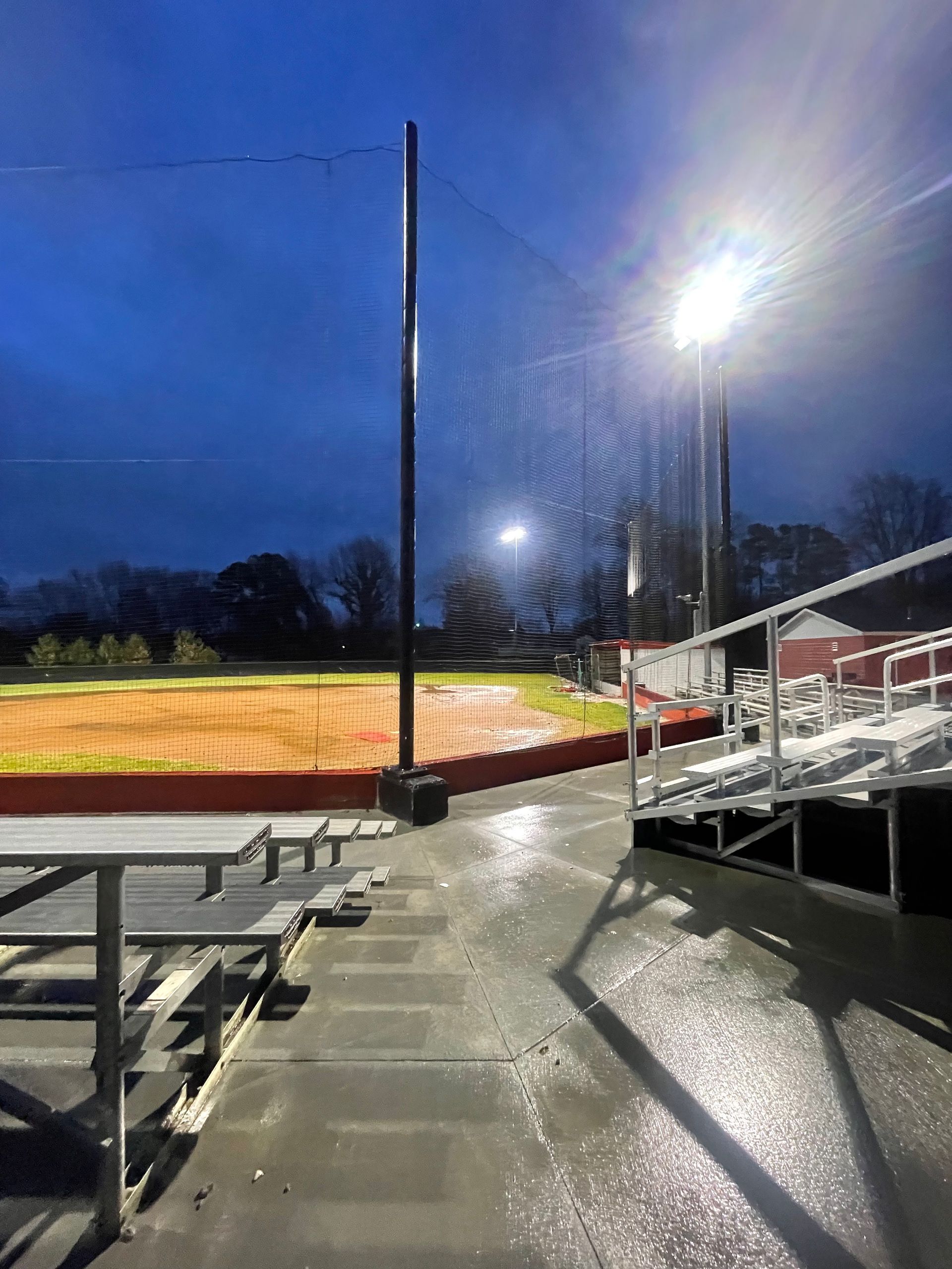 A baseball field with bleachers and a fence at night.